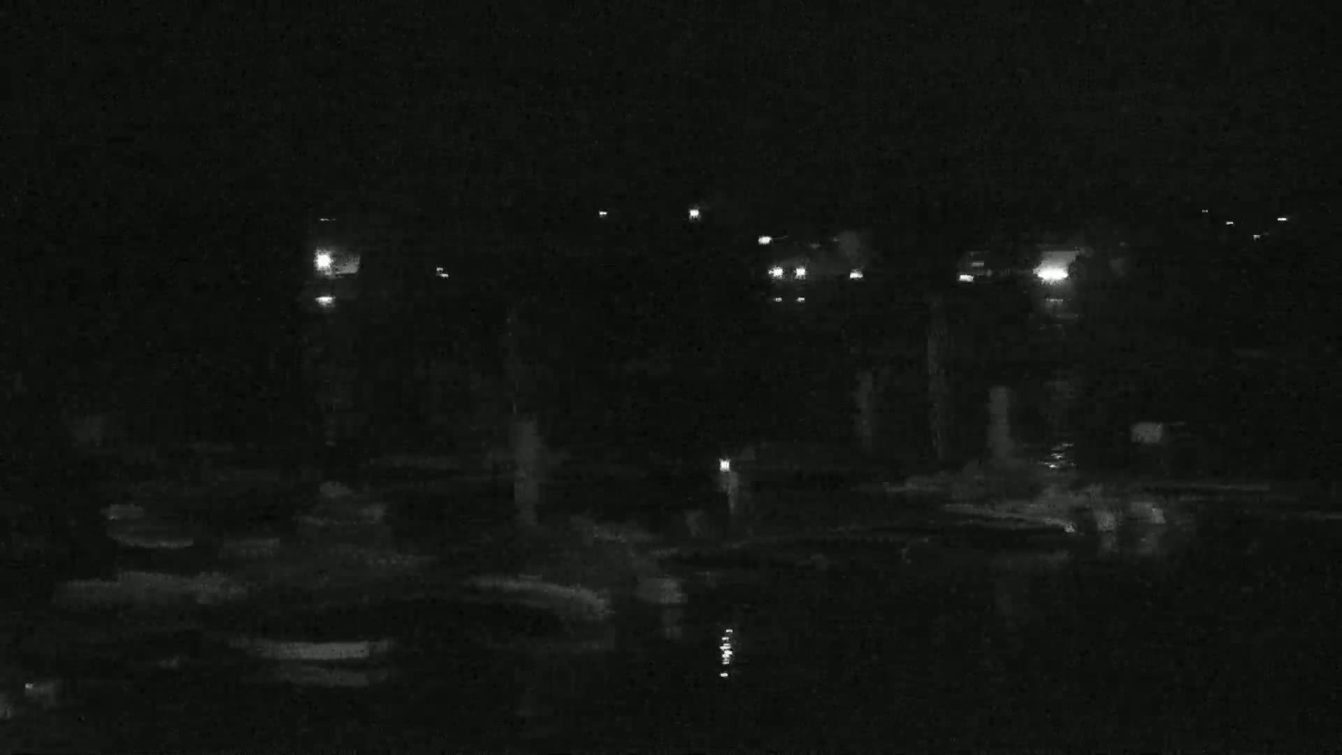 A nighttime, low-light view of a dark body of water reflecting scattered lights from a distant shoreline.