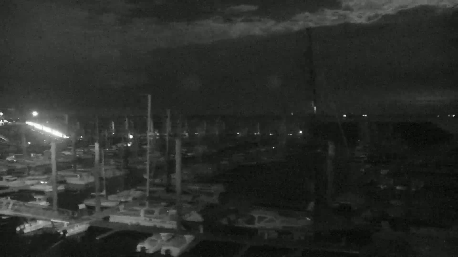A nighttime, overcast view of a marina filled with numerous boats and masts.