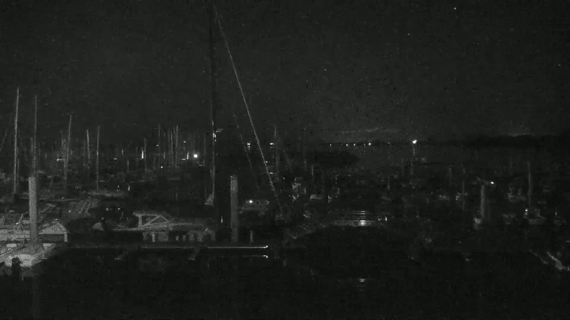 A nighttime, low-light view of a marina filled with numerous boats and masts under a dark, possibly cloudy sky.