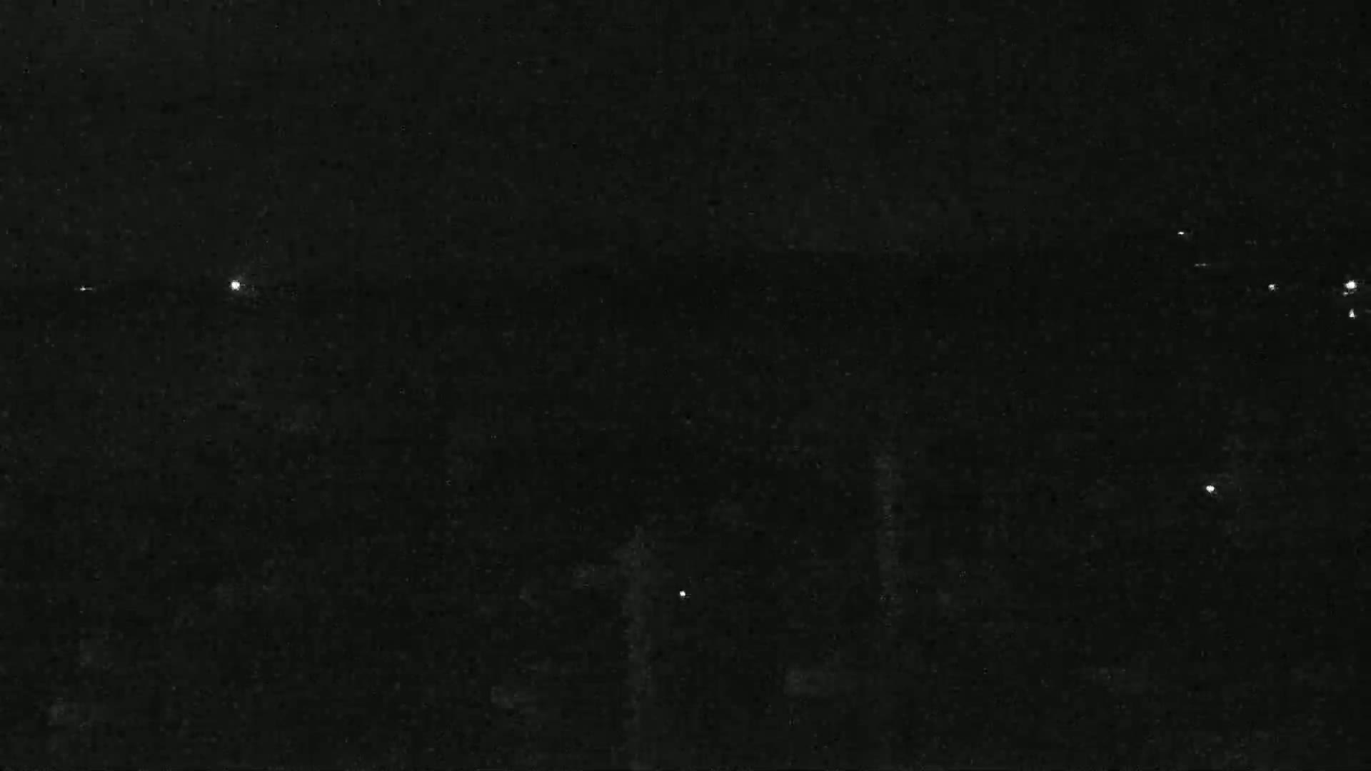 A dark, nighttime scene shows a few faint lights in the distance.