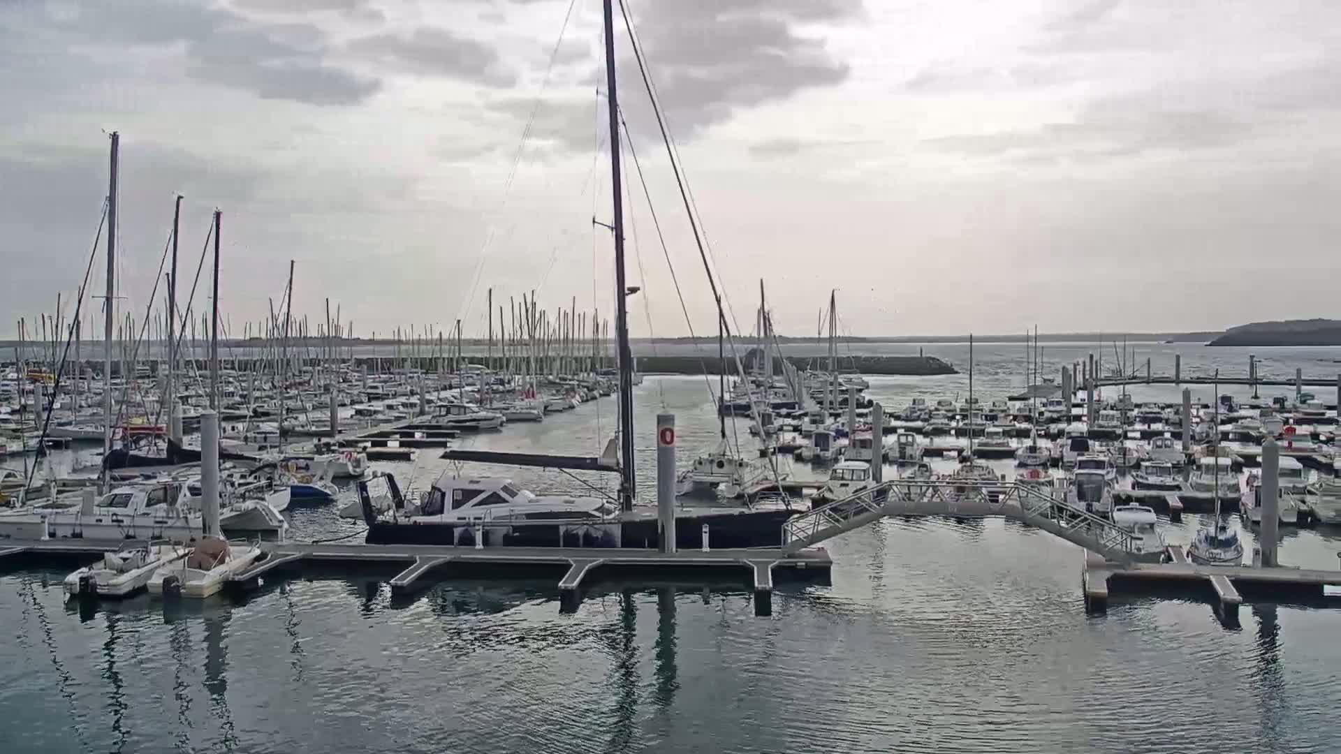 Many sailboats and motorboats are docked in a marina on an overcast day.