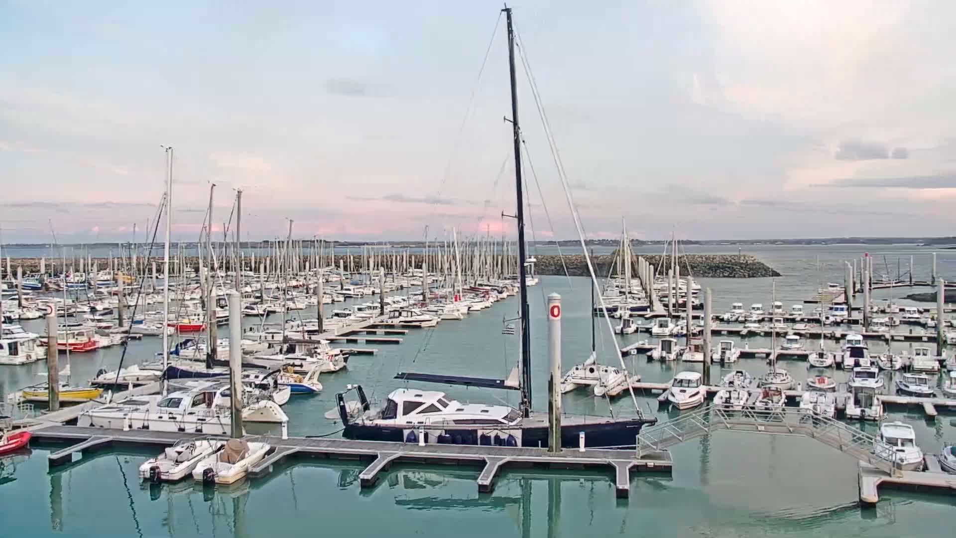 A calm marina filled with numerous sailboats and motorboats under a partly cloudy sky.