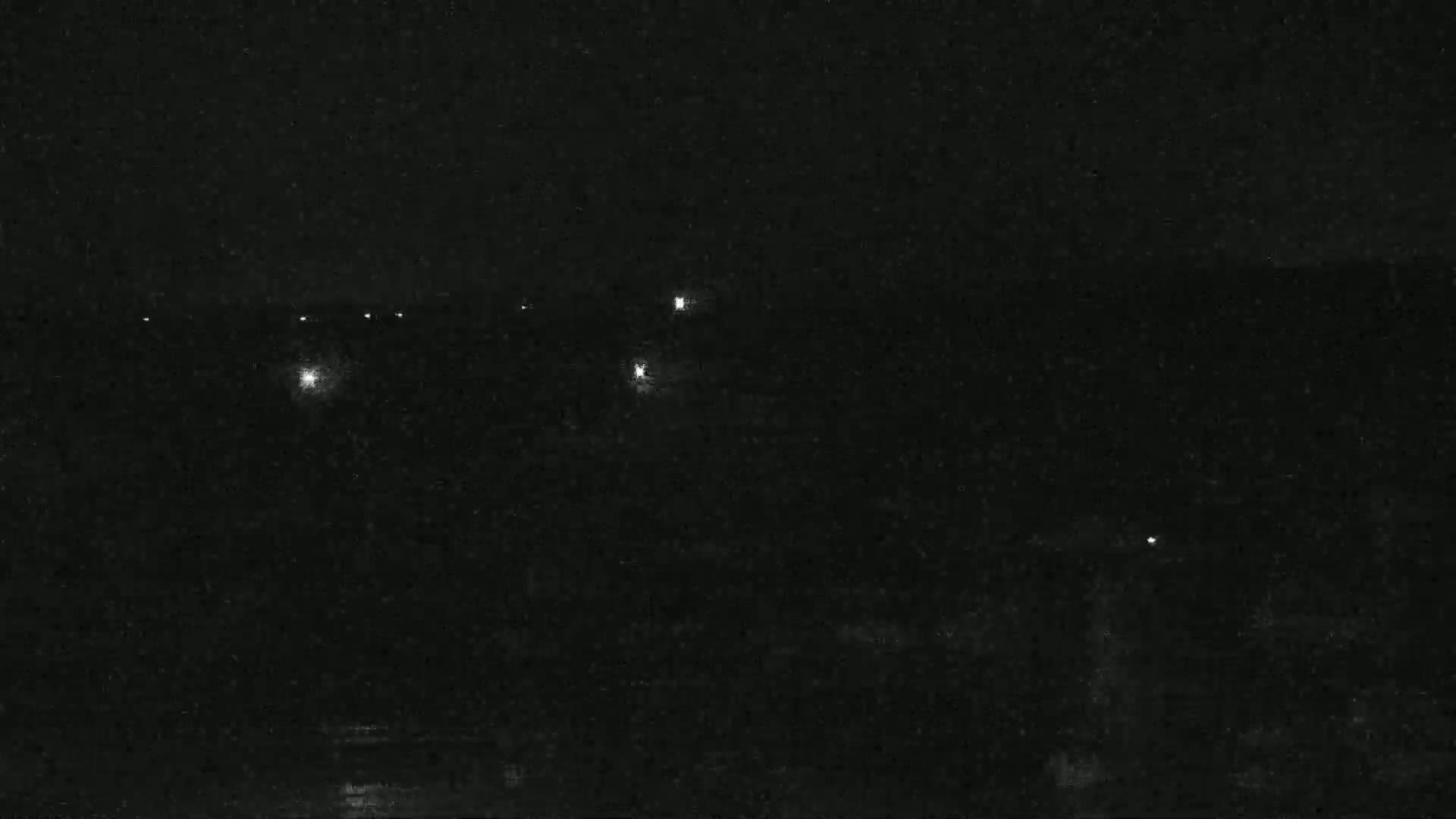 A dark nighttime scene shows several distant lights in the darkness.