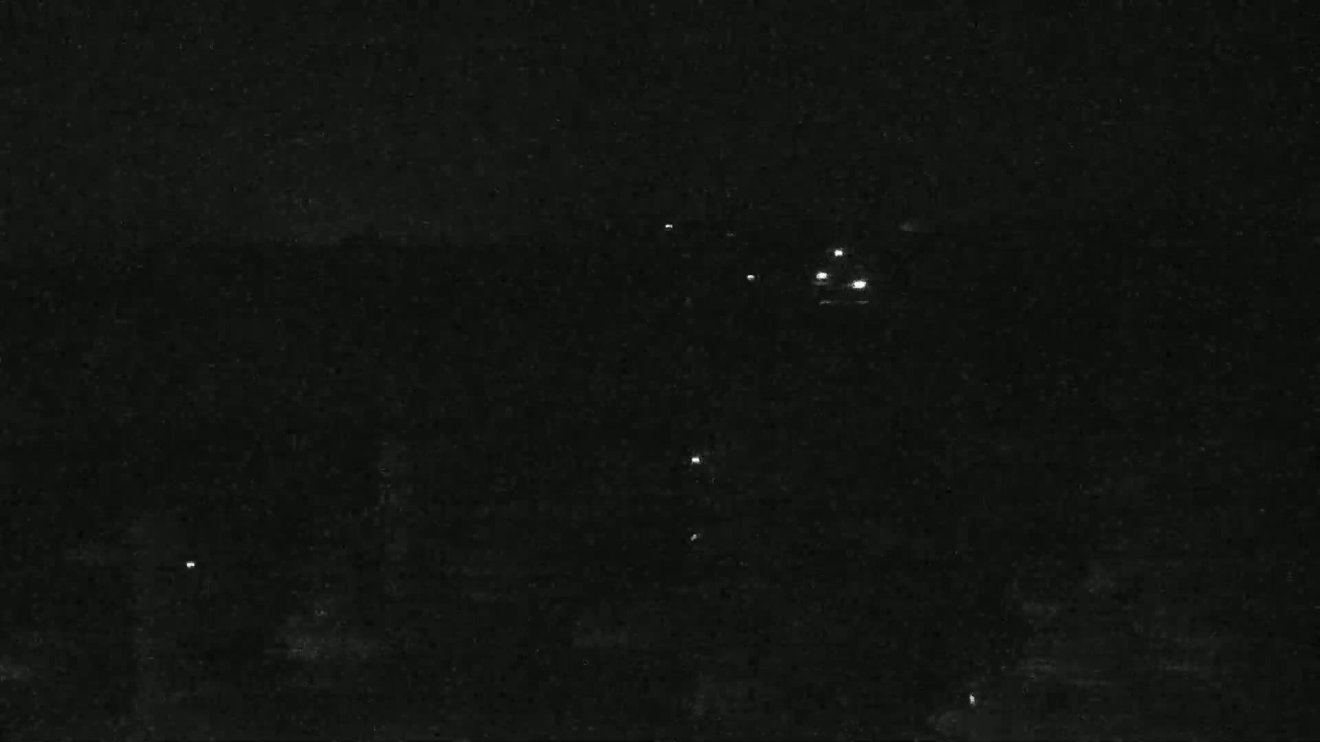A nighttime, dark scene shows a few distant lights scattered across a mostly black landscape.