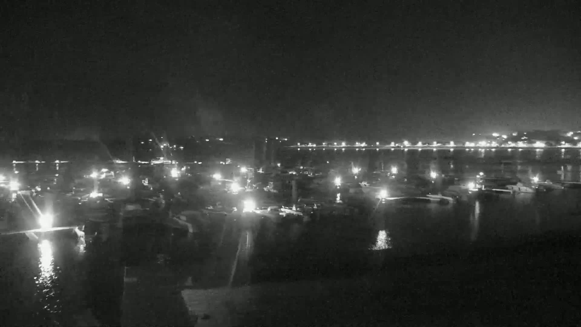 A nighttime, low-light view of a marina filled with numerous boats, illuminated by their own lights and those of a distant shore.