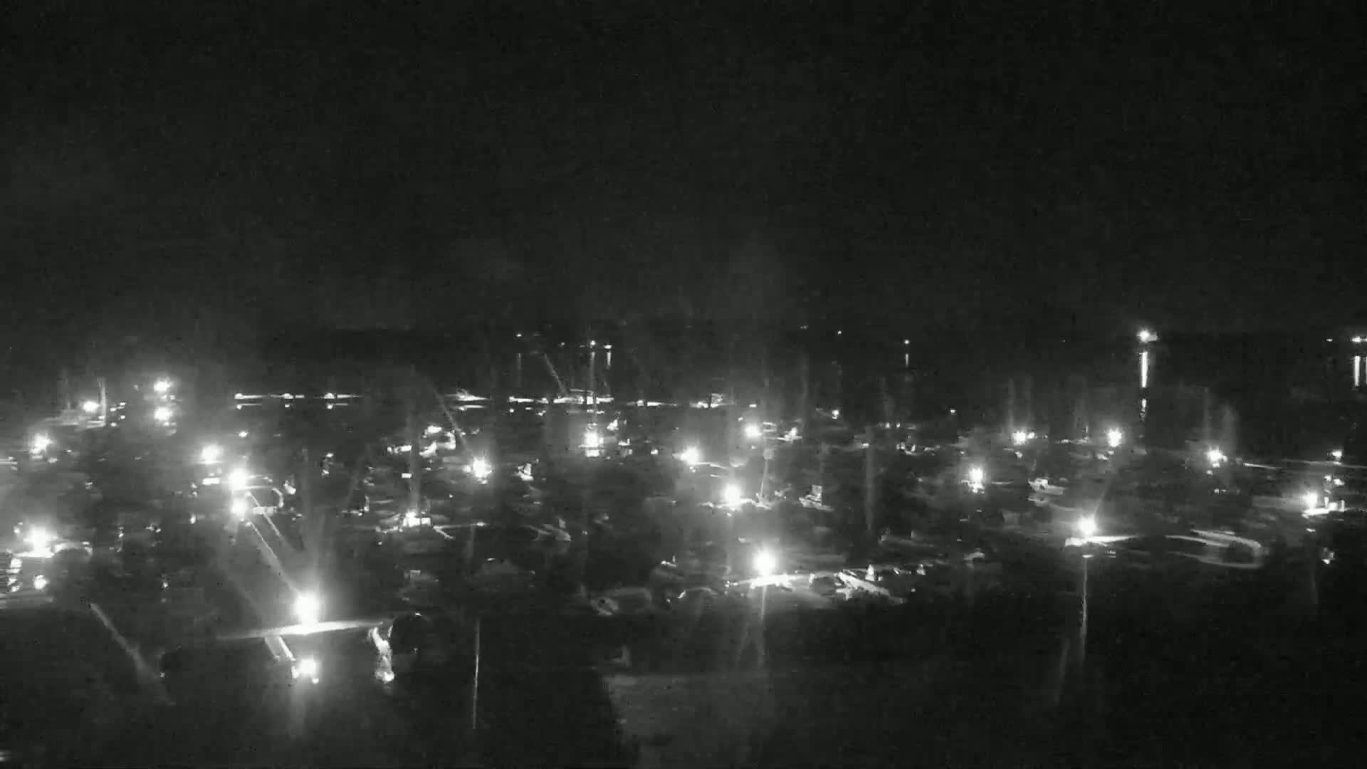 A nighttime, aerial view shows numerous lights scattered across a dark expanse, possibly a parking lot or a field with vehicles.