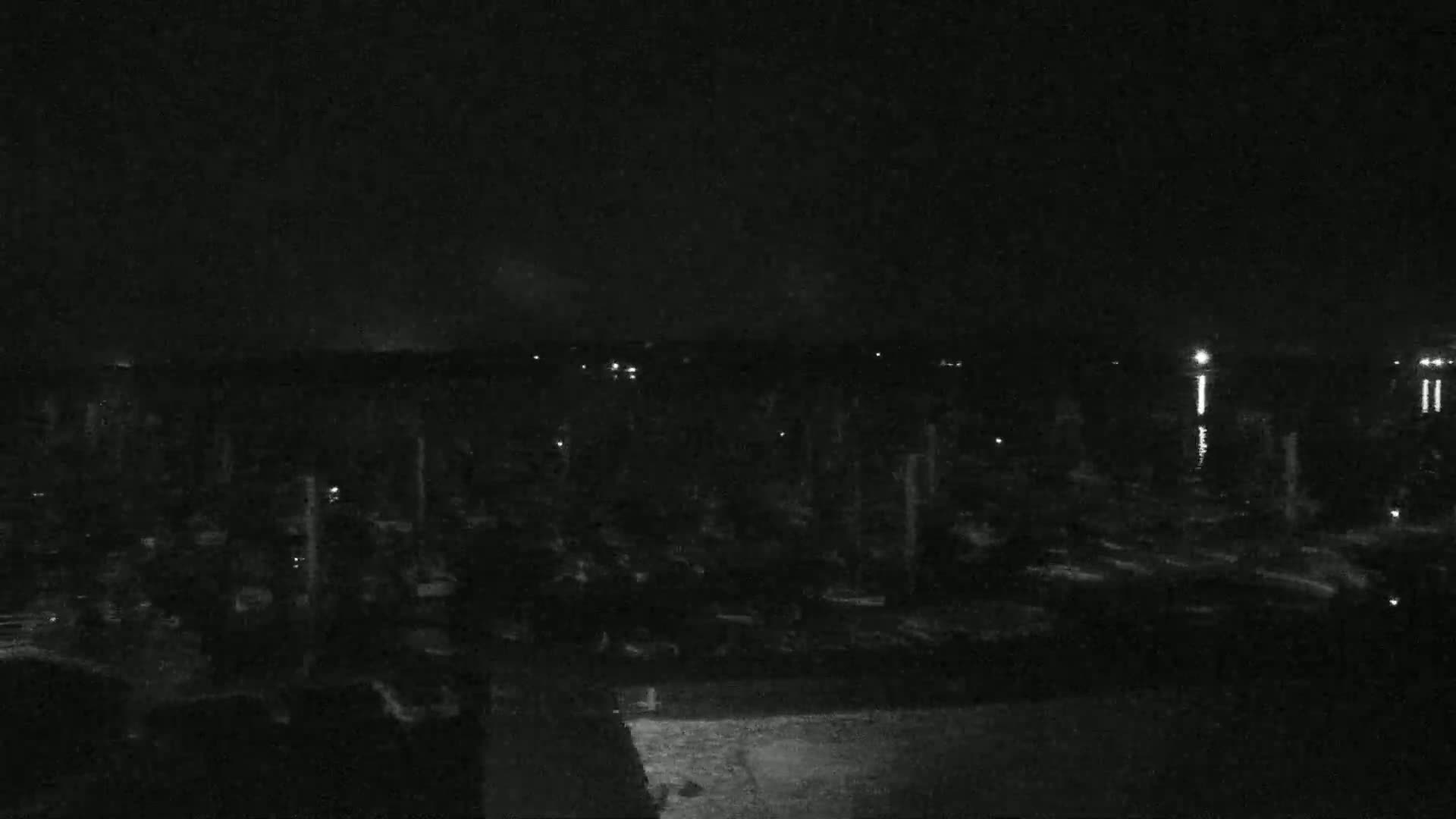 A nighttime, low-light view shows a marina filled with boats, and a dark body of water reflecting faint lights.