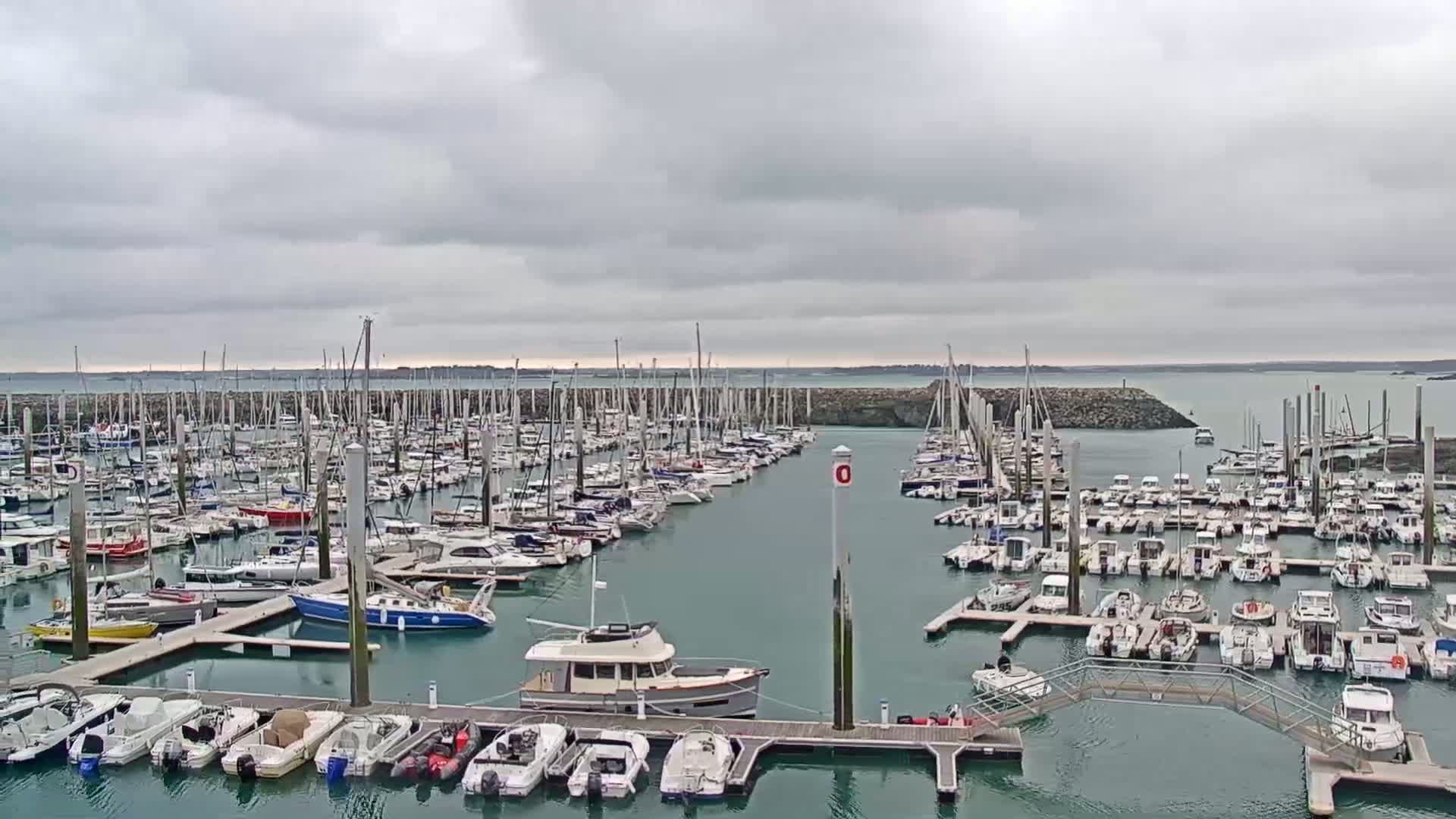 A marina filled with numerous sailboats and motorboats under a cloudy sky.