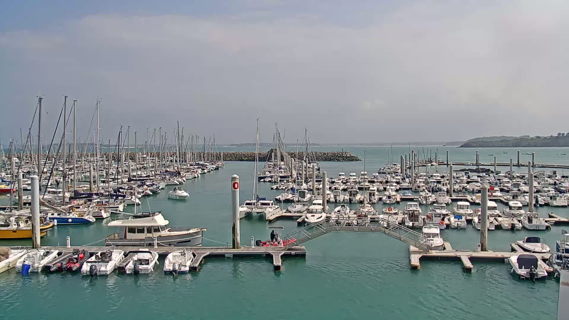 A marina filled with numerous sailboats and motorboats is shown under a partly cloudy sky.