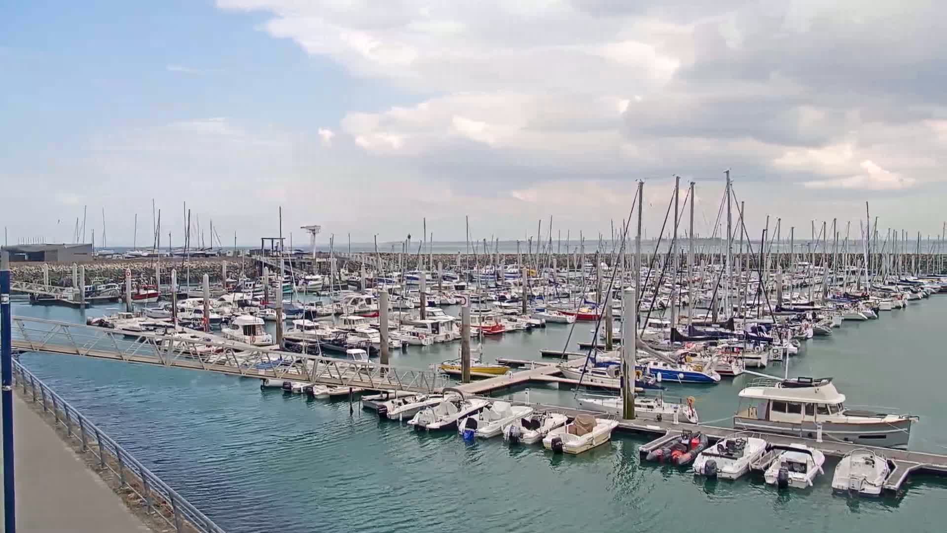 A marina filled with numerous sailboats and motorboats under a partly cloudy sky.