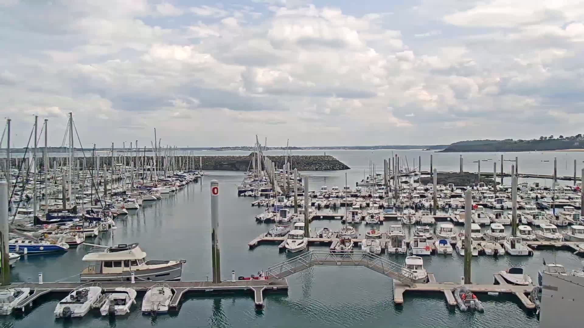 A large marina filled with many sailboats and motorboats is shown under a partly cloudy sky.