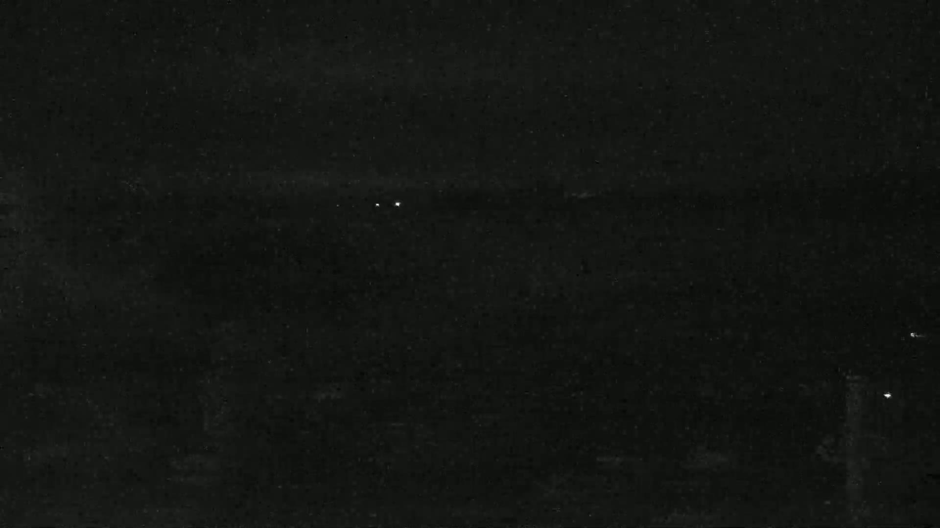 A dark, nighttime scene shows a few faint lights in the distance.
