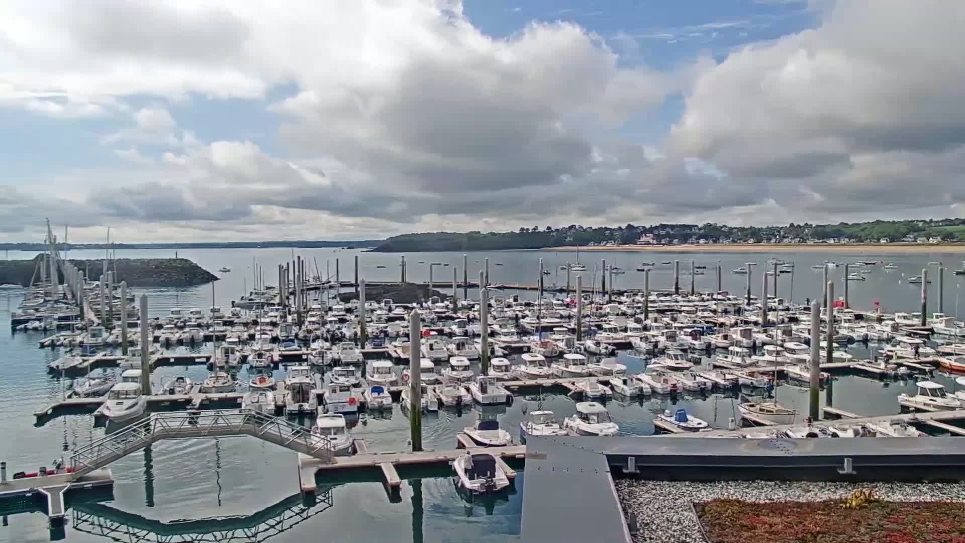 A large marina filled with numerous boats is situated on calm water under a partly cloudy sky.