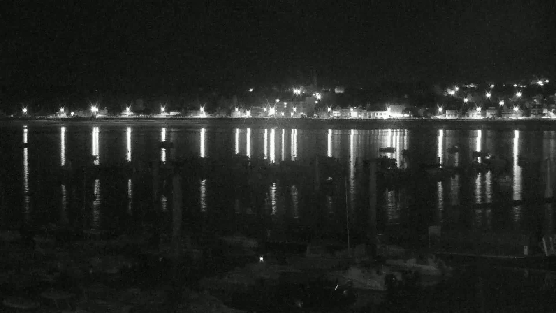 A nighttime view of a calm body of water reflecting the lights of a town across the shore.