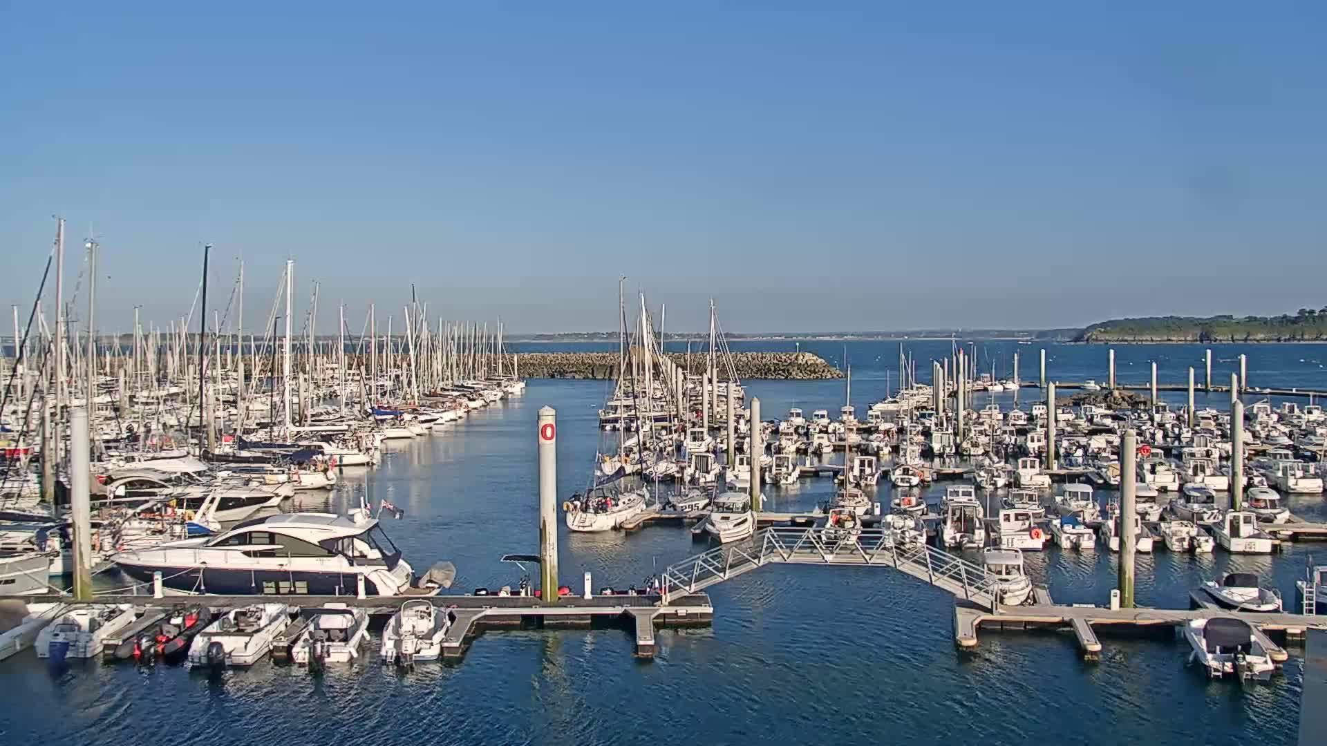 A marina filled with numerous sailboats and motorboats is seen on a sunny day.