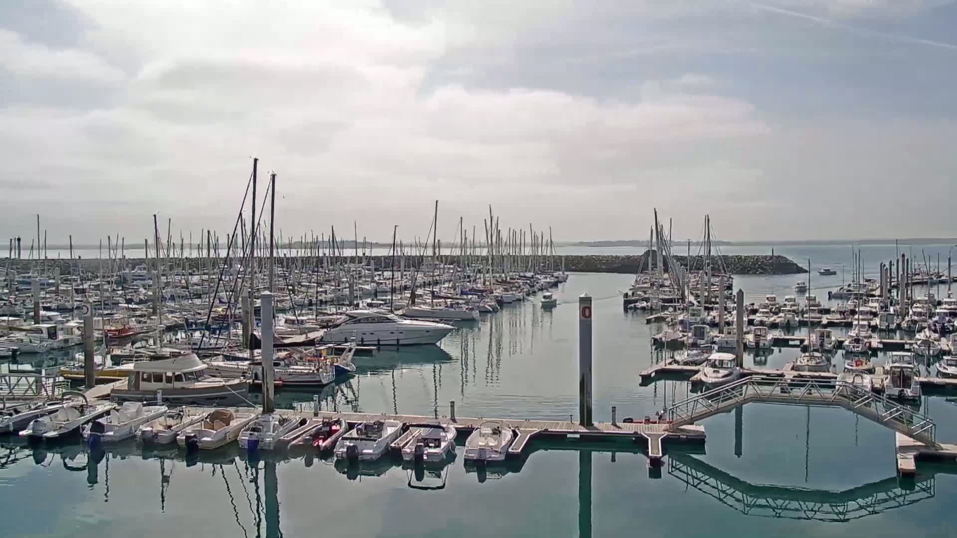 A marina filled with numerous sailboats and motorboats is shown on a partly cloudy day.