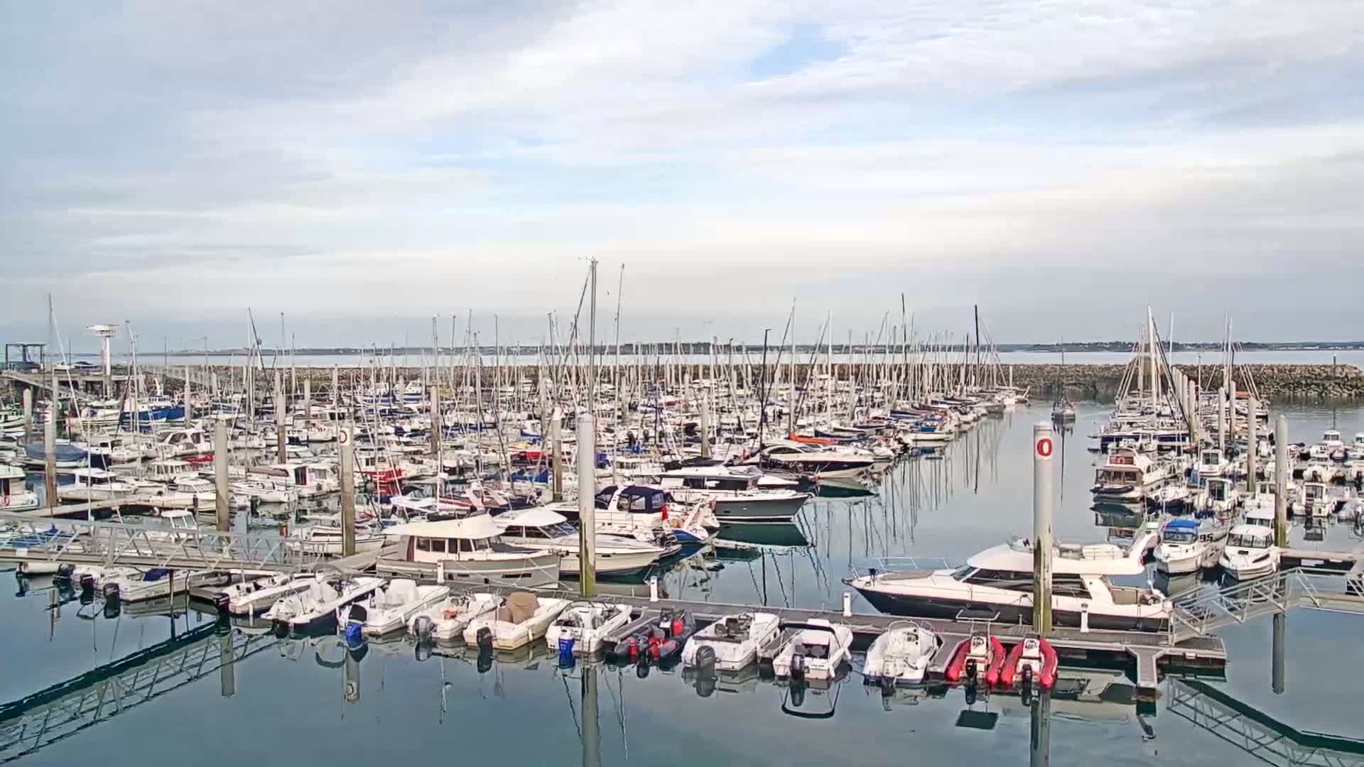 A marina filled with numerous sailboats and motorboats under a mostly cloudy sky.