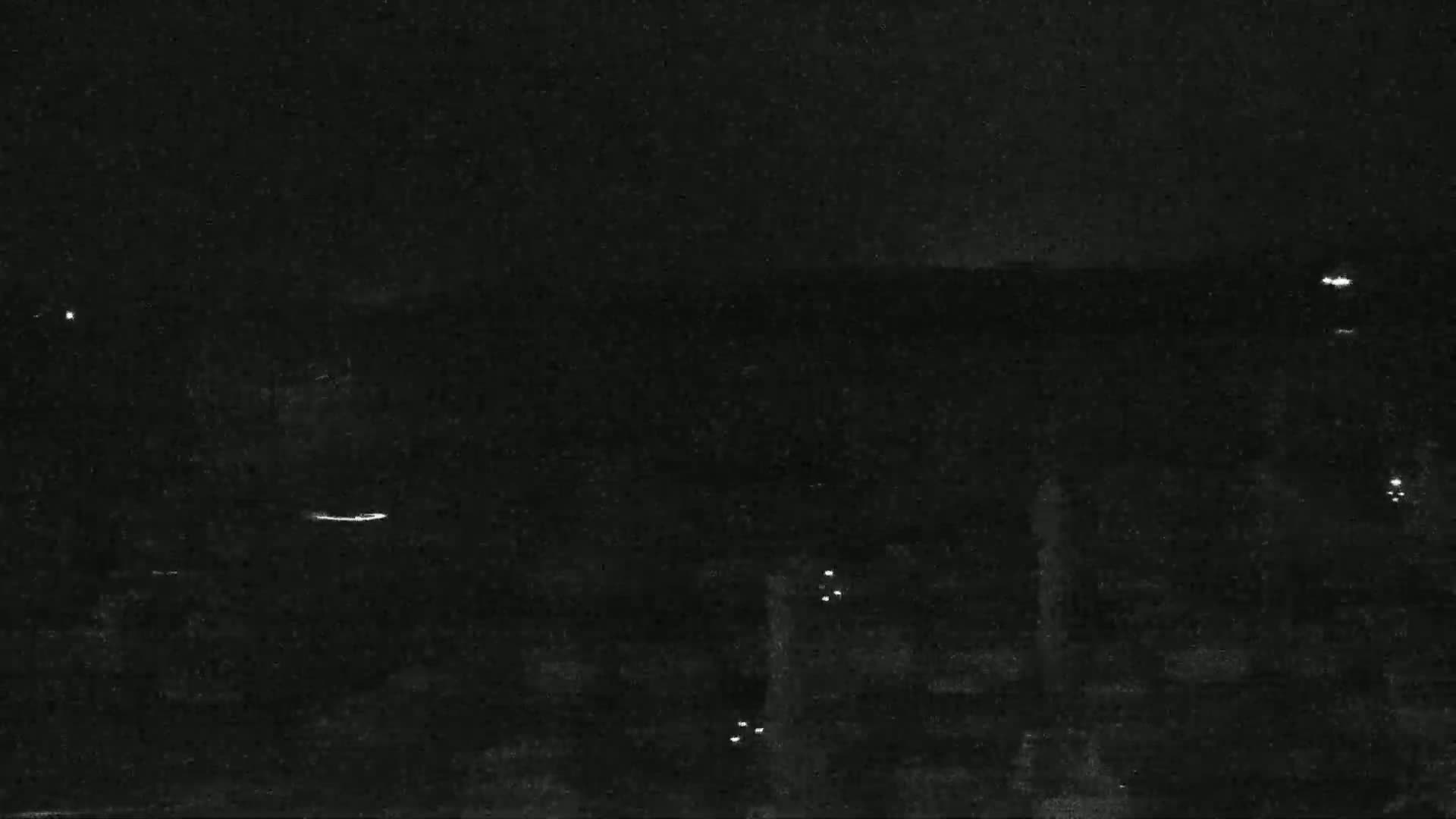 A nighttime, low-light view shows a dark landscape with a few scattered points of light.