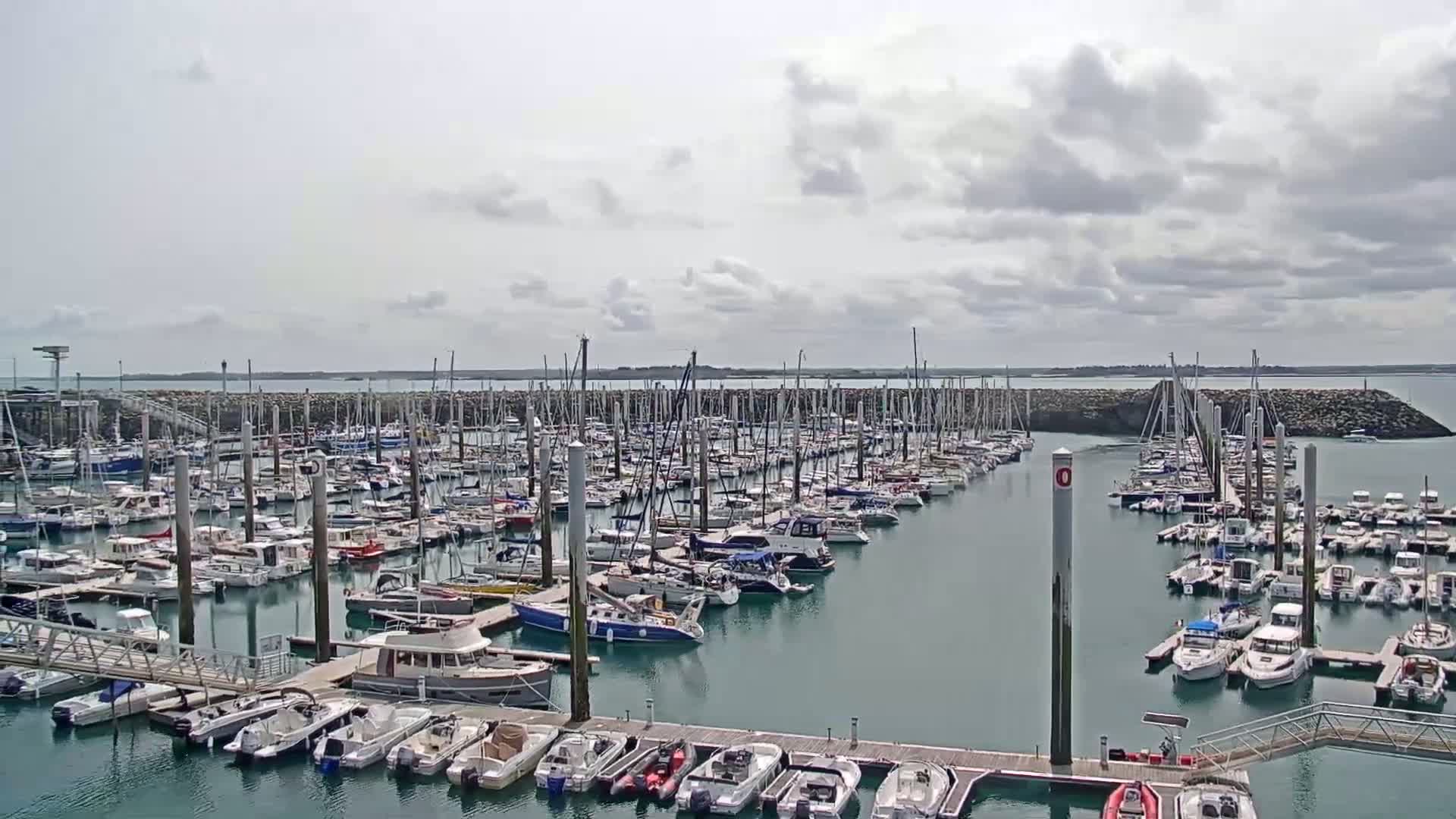 A large marina filled with numerous sailboats and motorboats under a partly cloudy sky.