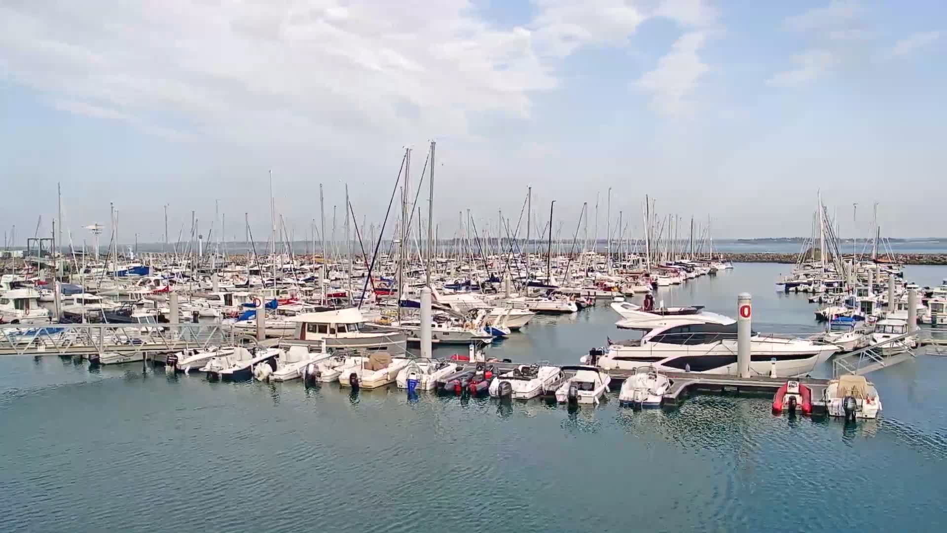 A large marina filled with numerous sailboats and motorboats under a partly cloudy sky.