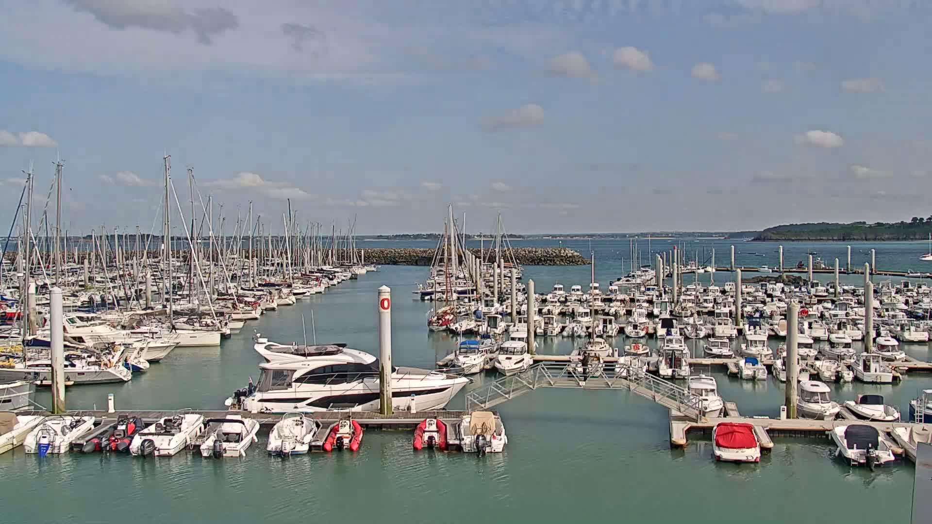 A marina filled with numerous sailboats and motorboats is shown on a partly cloudy day.