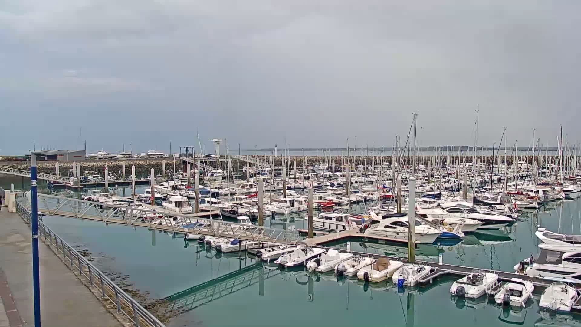 A marina filled with numerous sailboats and motorboats under an overcast sky.