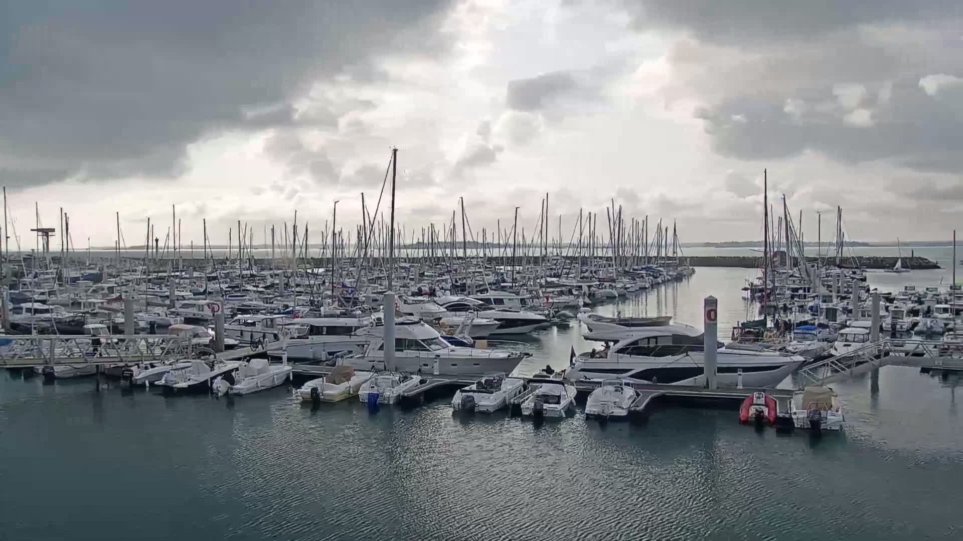 Many yachts and motorboats are docked in a marina under a cloudy sky.