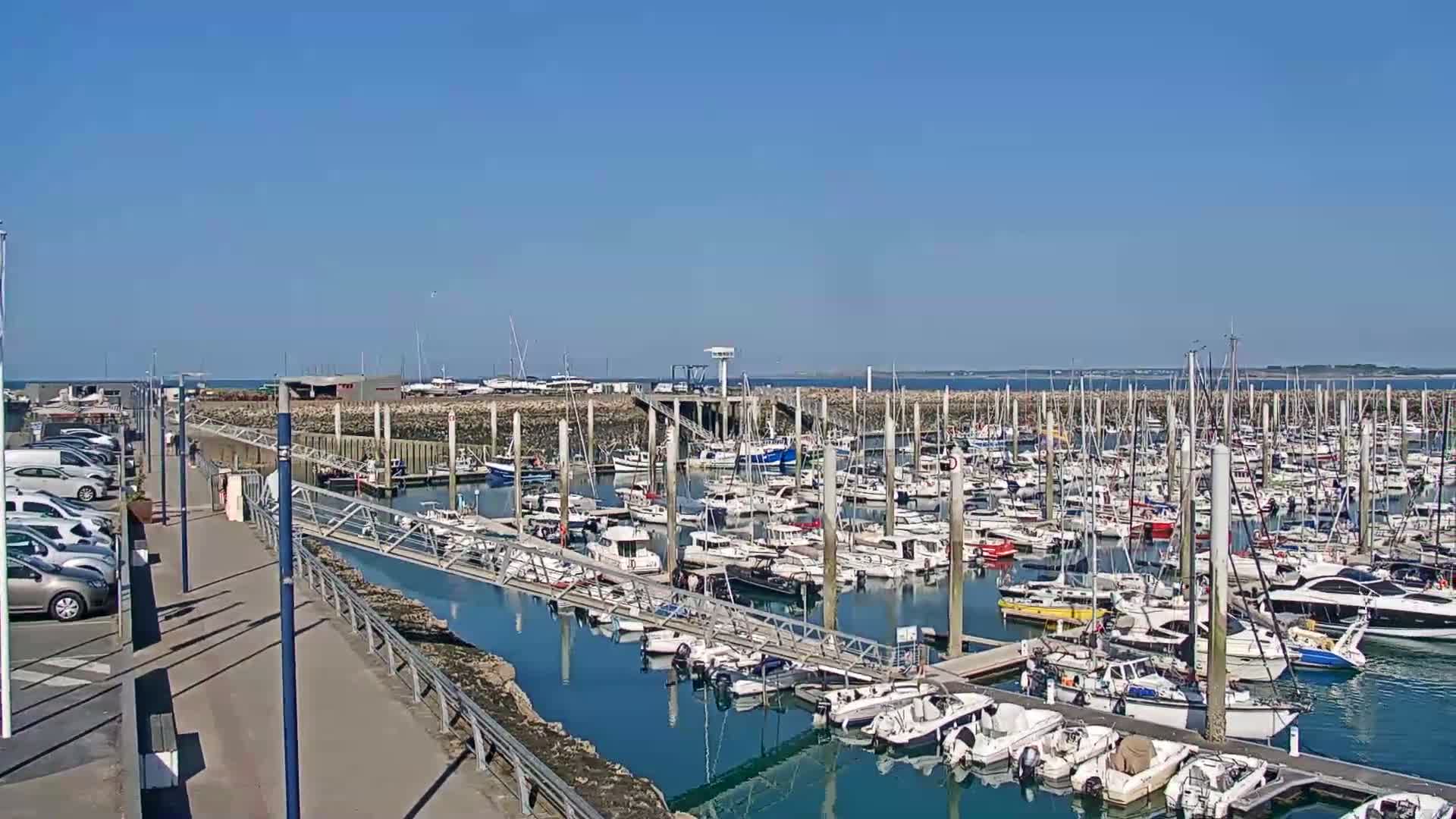 A marina filled with numerous boats of various sizes is shown on a sunny day.