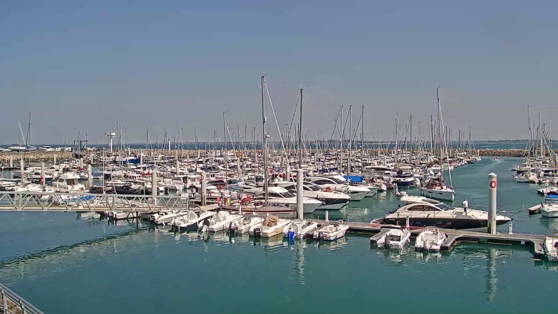 A marina filled with numerous sailboats and motorboats is shown on a sunny day.
