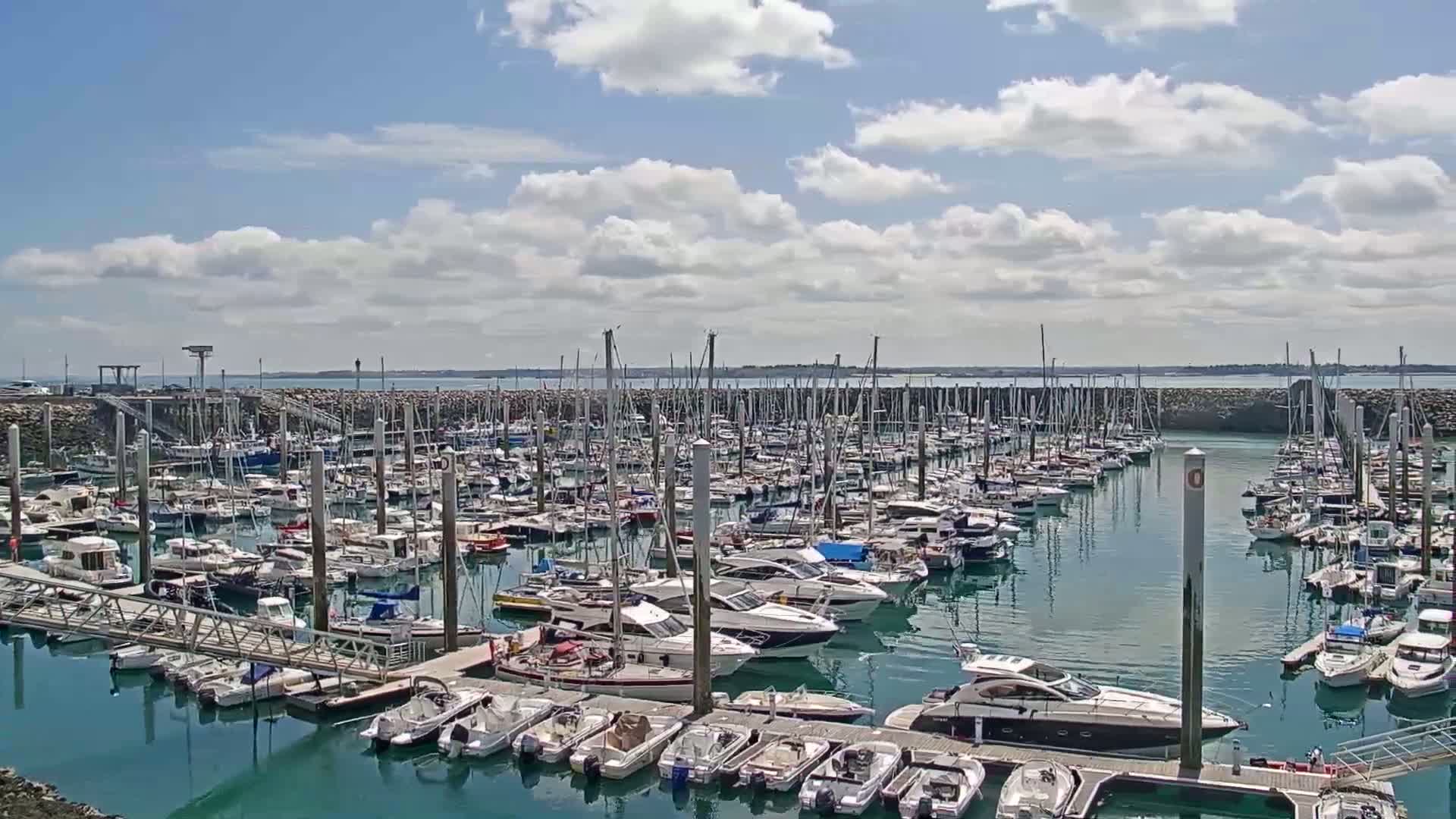 A large marina filled with numerous sailboats and motorboats under a partly cloudy sky.