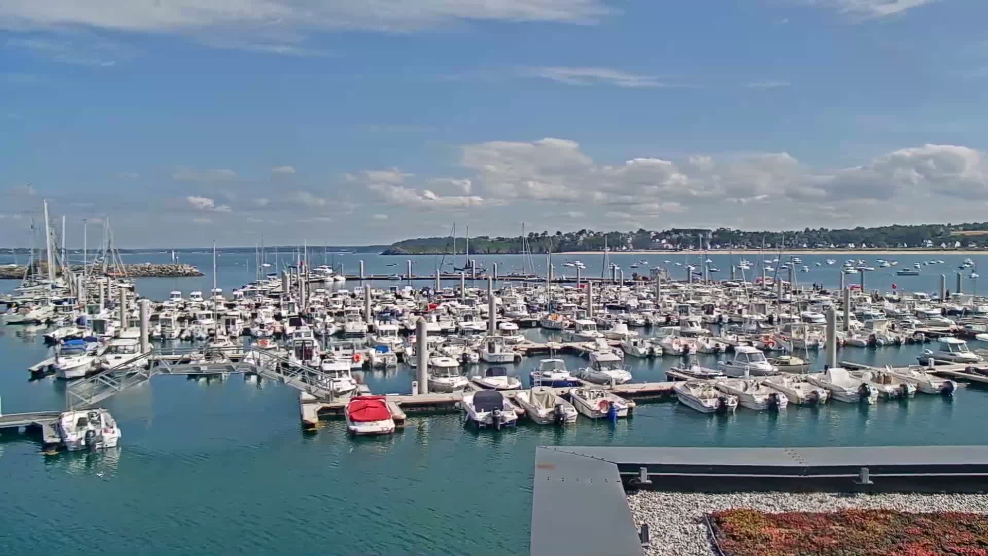 A large marina filled with numerous boats is situated on a calm, blue body of water under a partly cloudy sky.