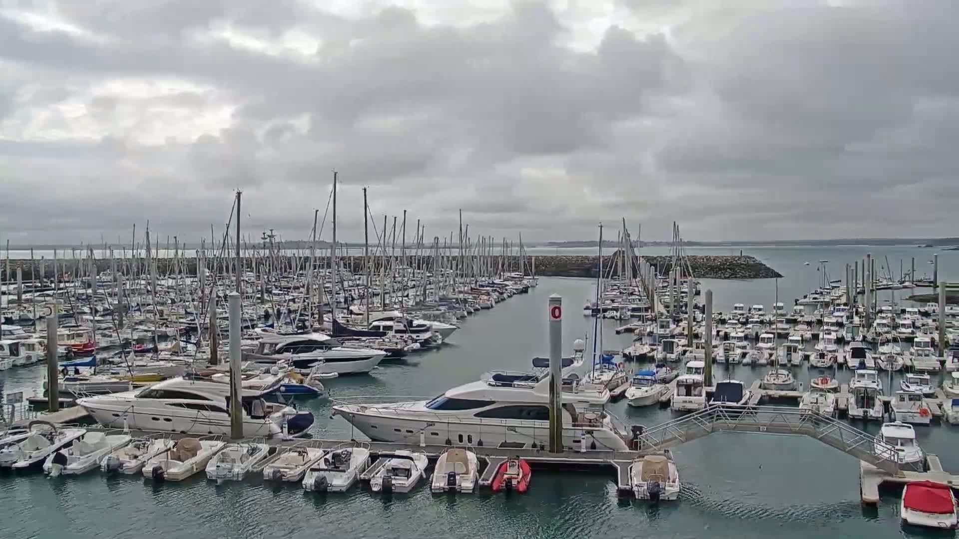 A large marina filled with many sailboats and motorboats is shown under a cloudy sky.