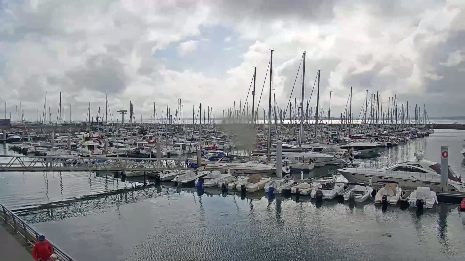 A marina filled with numerous sailboats and motorboats under a cloudy sky.