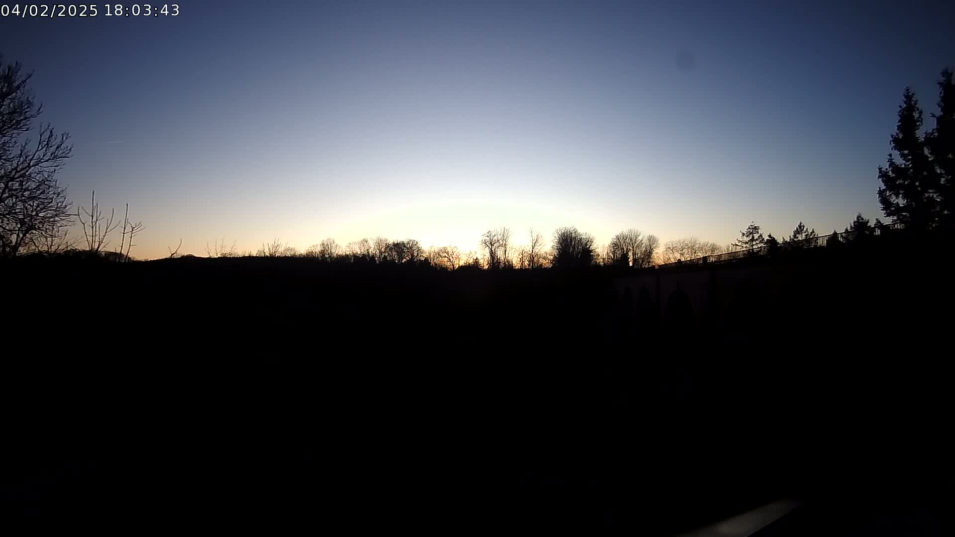 A silhouetted line of trees and a structure are visible against a clear twilight sky.