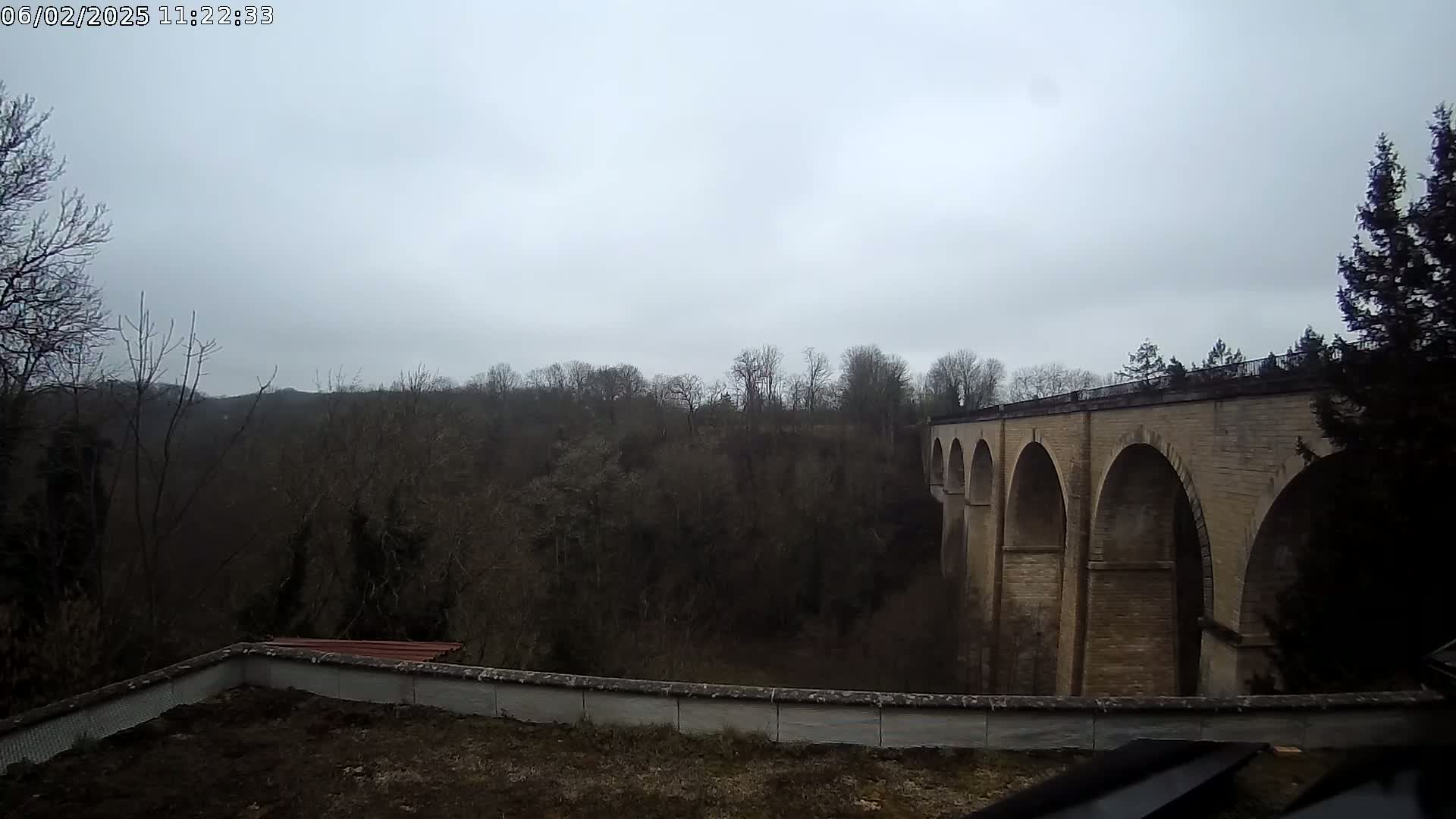 A stone viaduct stretches across a valley of leafless trees under a cloudy sky.