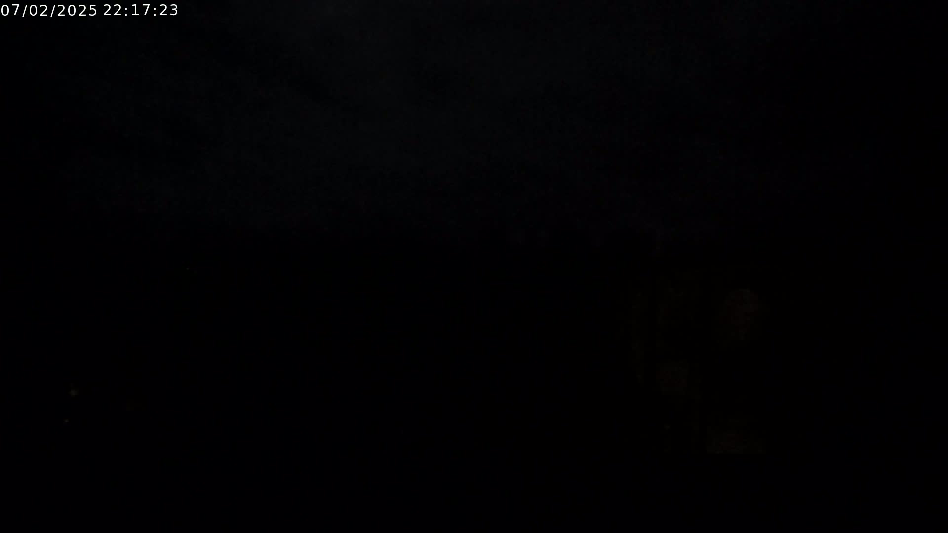 A dark, nighttime scene shows a dimly lit area on the right with an indiscernible object, and a very dark, possibly cloudy sky.