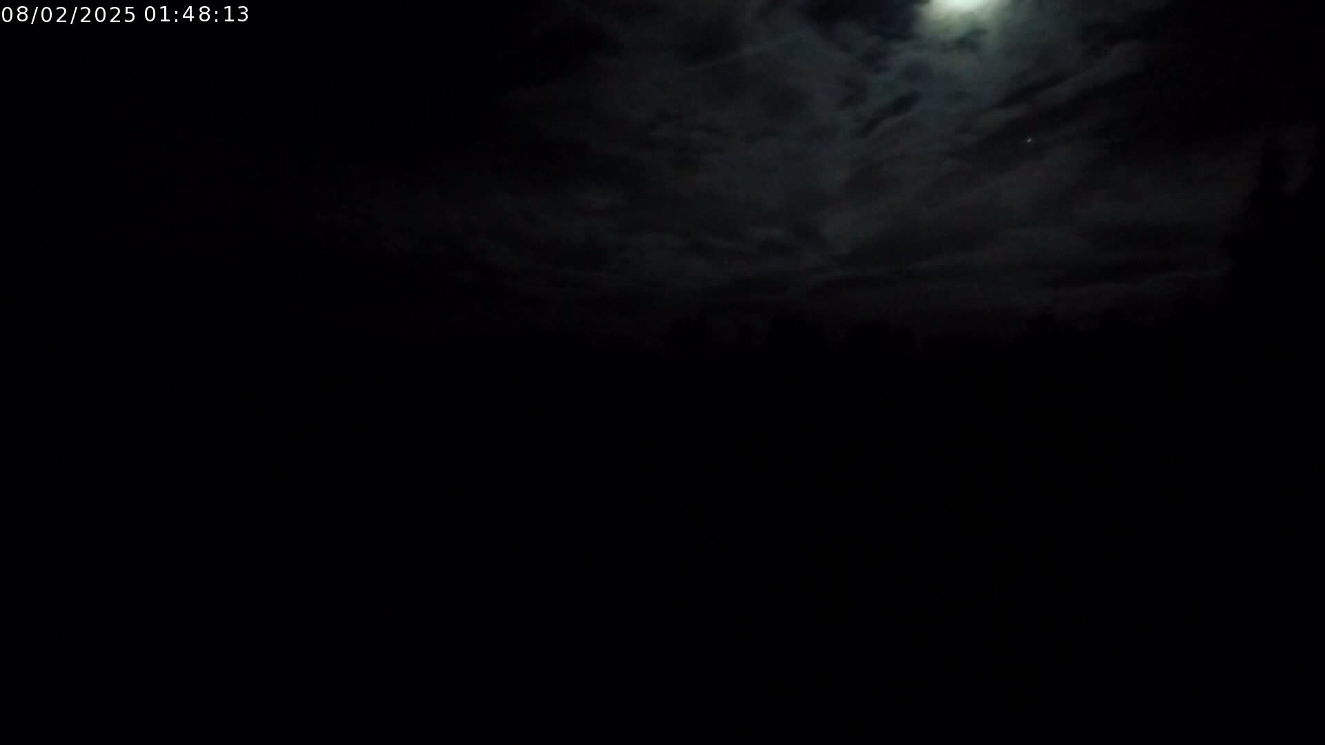 A nighttime scene shows a bright moon partially obscured by dark clouds above a silhouetted landscape.