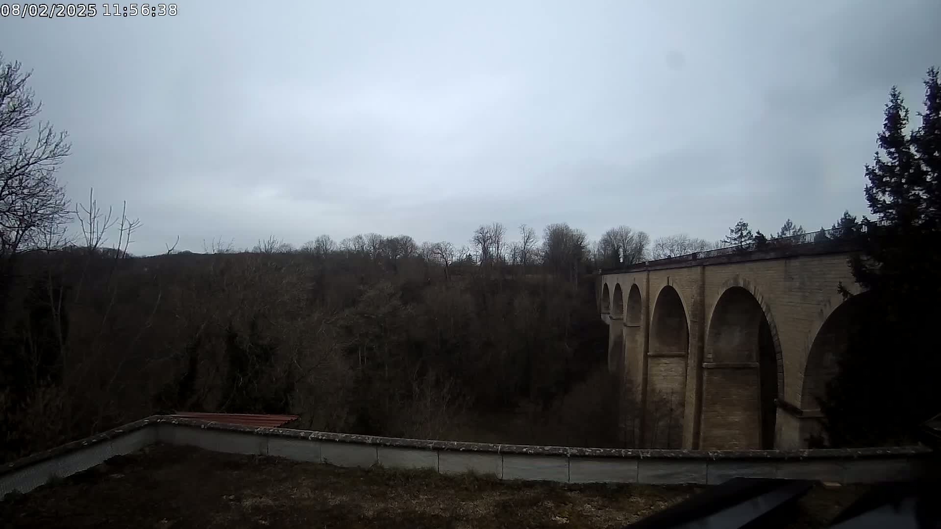A stone viaduct stretches across a valley of bare winter trees under an overcast sky.