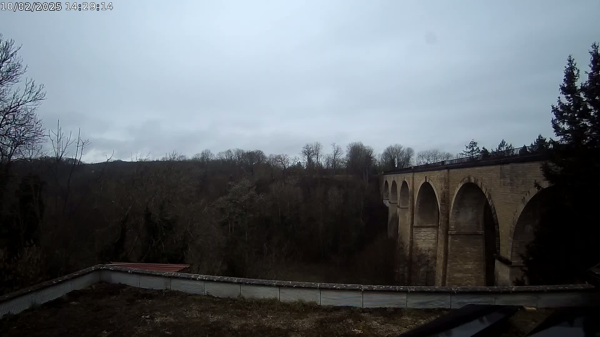 A stone viaduct with multiple arches stretches across a wooded valley under an overcast sky.
