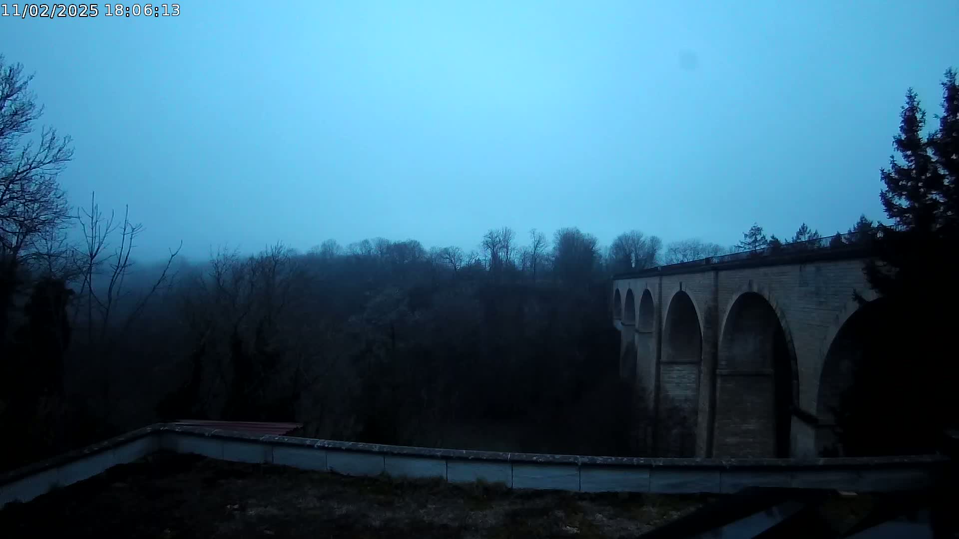 A stone viaduct is visible in the hazy, twilight sky above a dark, wooded valley.