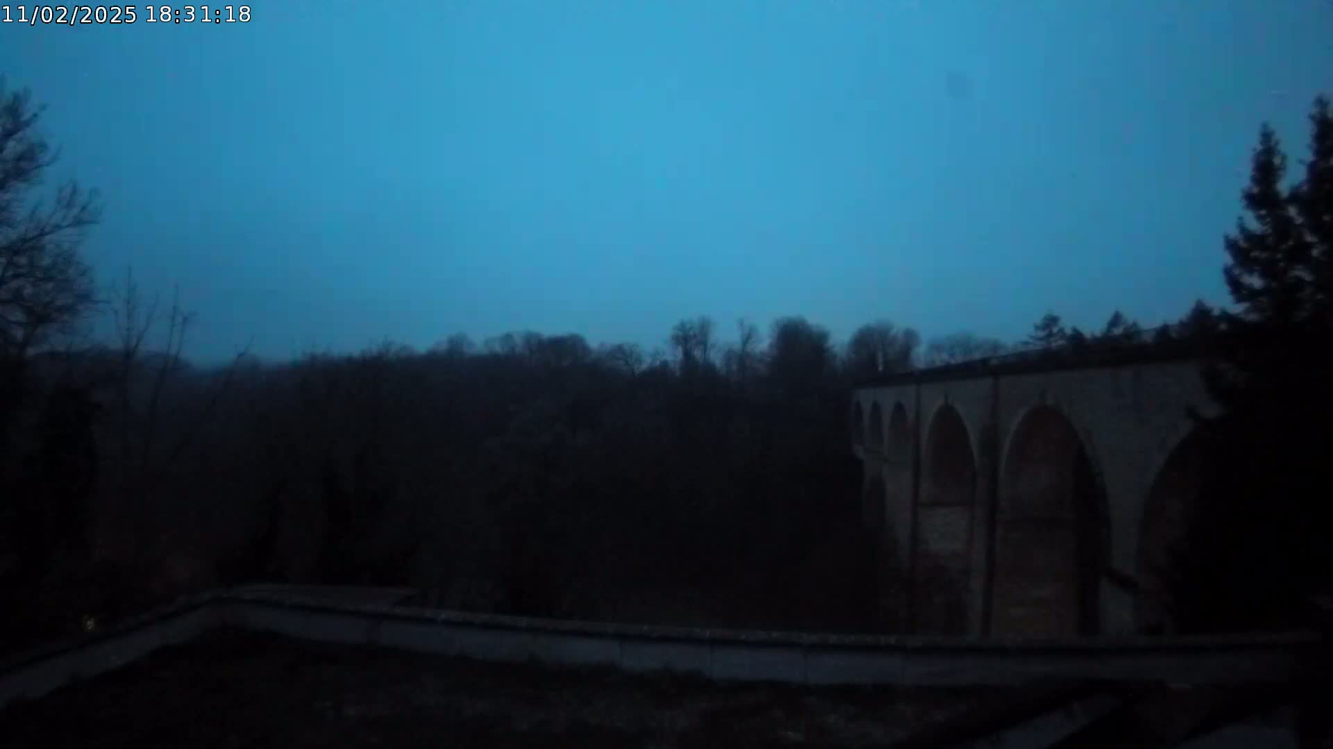 A stone viaduct with multiple arches is seen at twilight under a dark blue, hazy sky.
