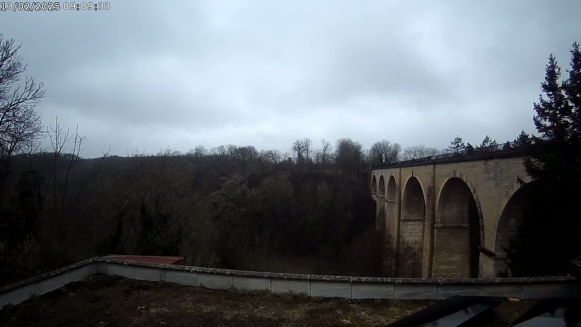 A stone viaduct stretches across a wooded valley under a cloudy sky.