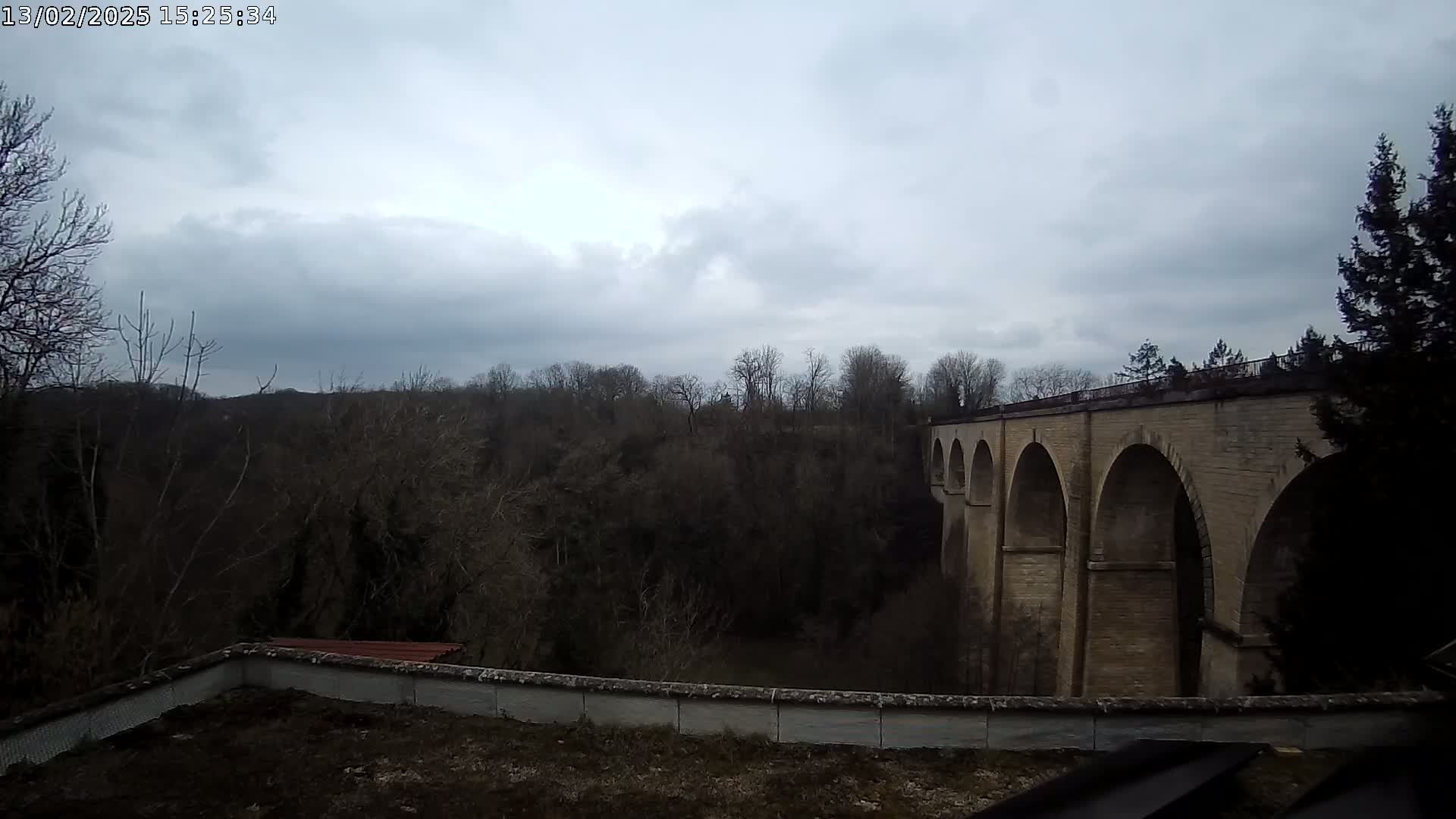 A stone viaduct with multiple arches stretches across a wooded valley under a cloudy sky.