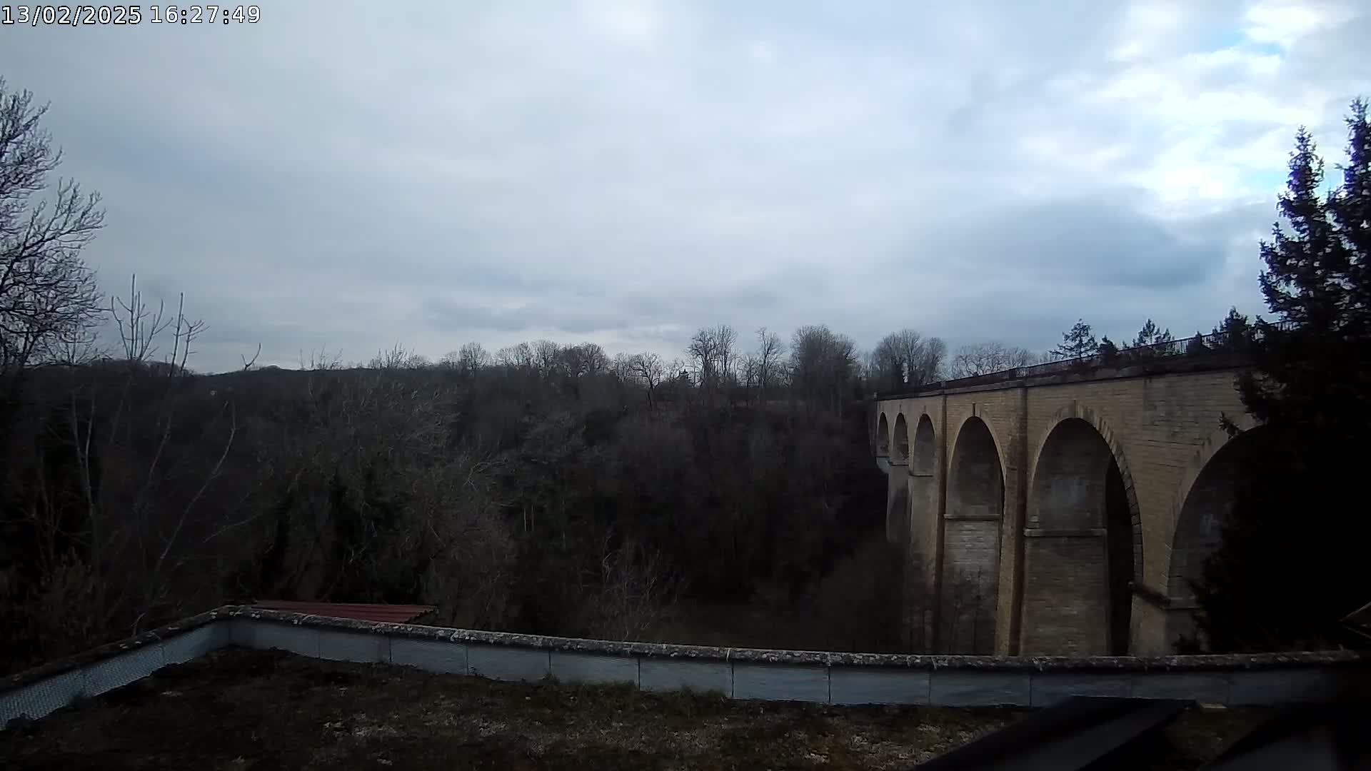 A stone viaduct stretches across a valley of leafless trees under a cloudy sky.