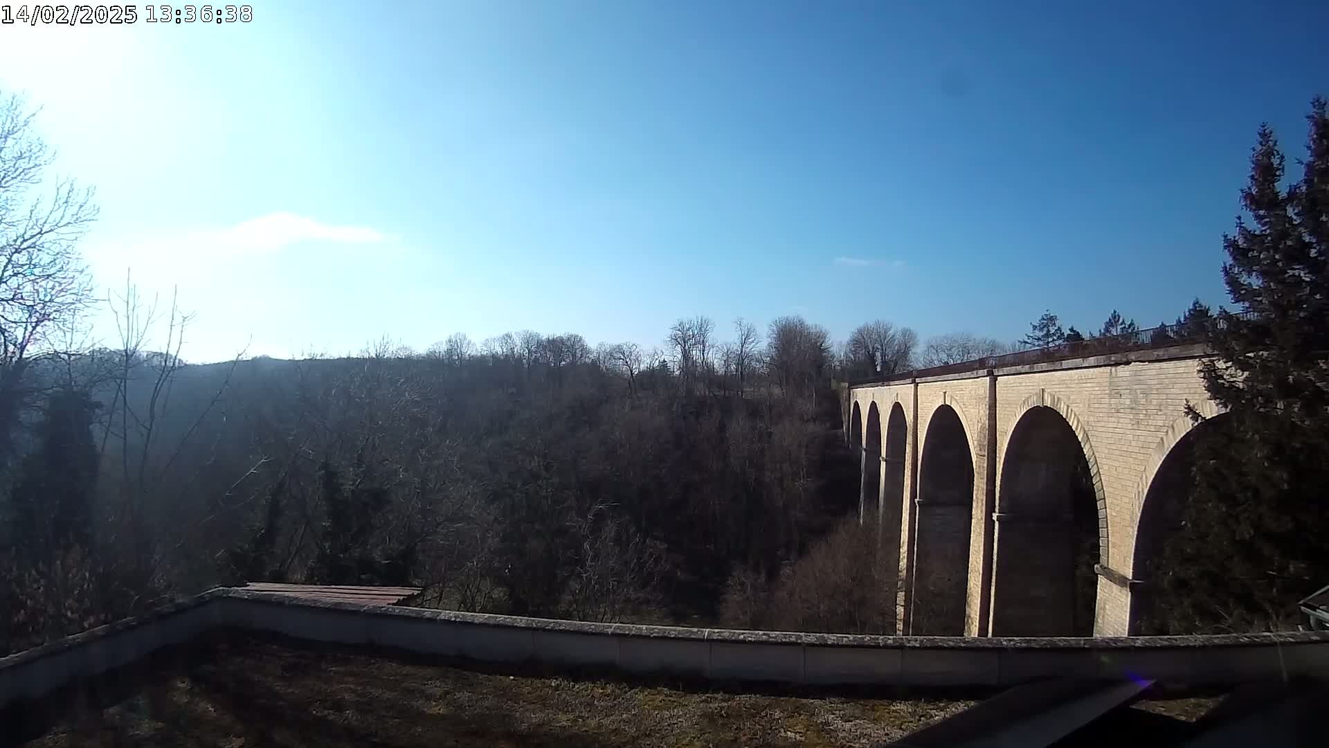A stone arched viaduct stretches across a valley of leafless trees under a clear blue sky.