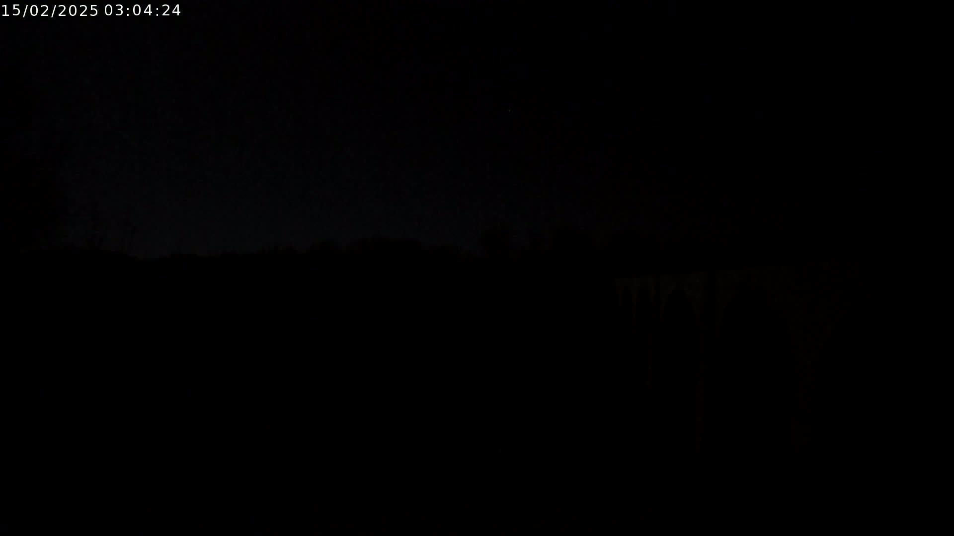 A very dark nighttime scene shows a silhouetted landscape under a mostly clear sky.