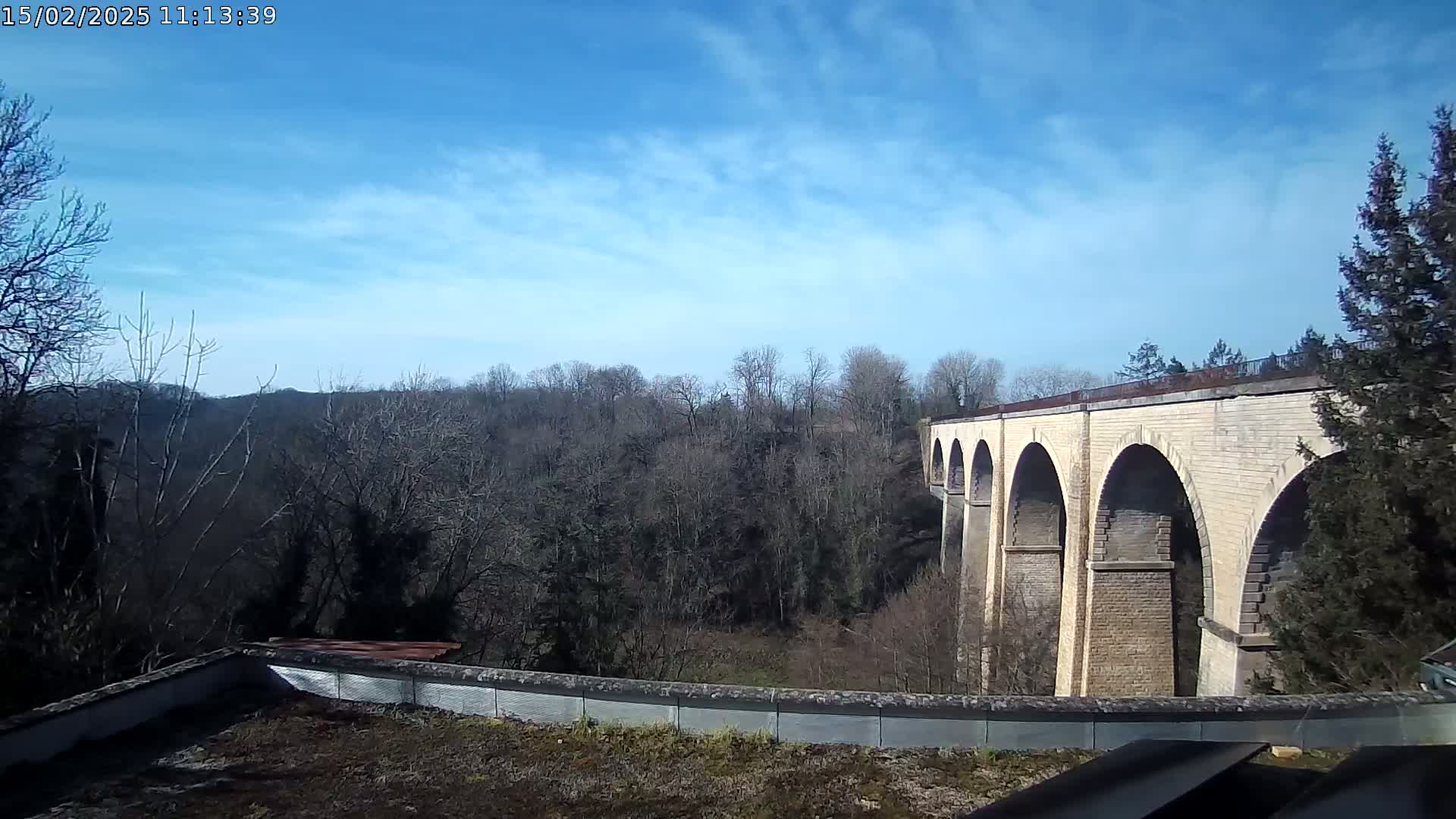 A stone viaduct stretches across a valley of leafless trees under a mostly clear, bright blue sky.