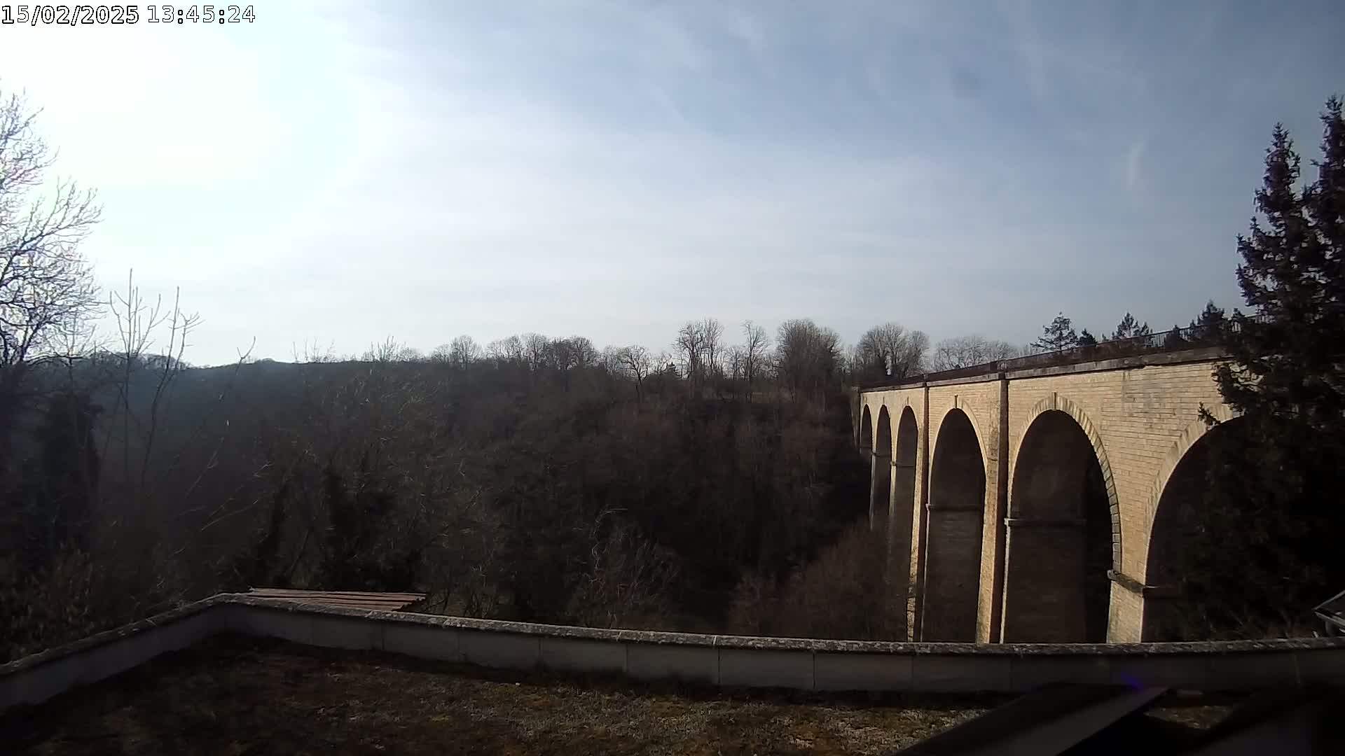 A brick viaduct stretches across a valley of leafless trees under a mostly clear, bright sky.