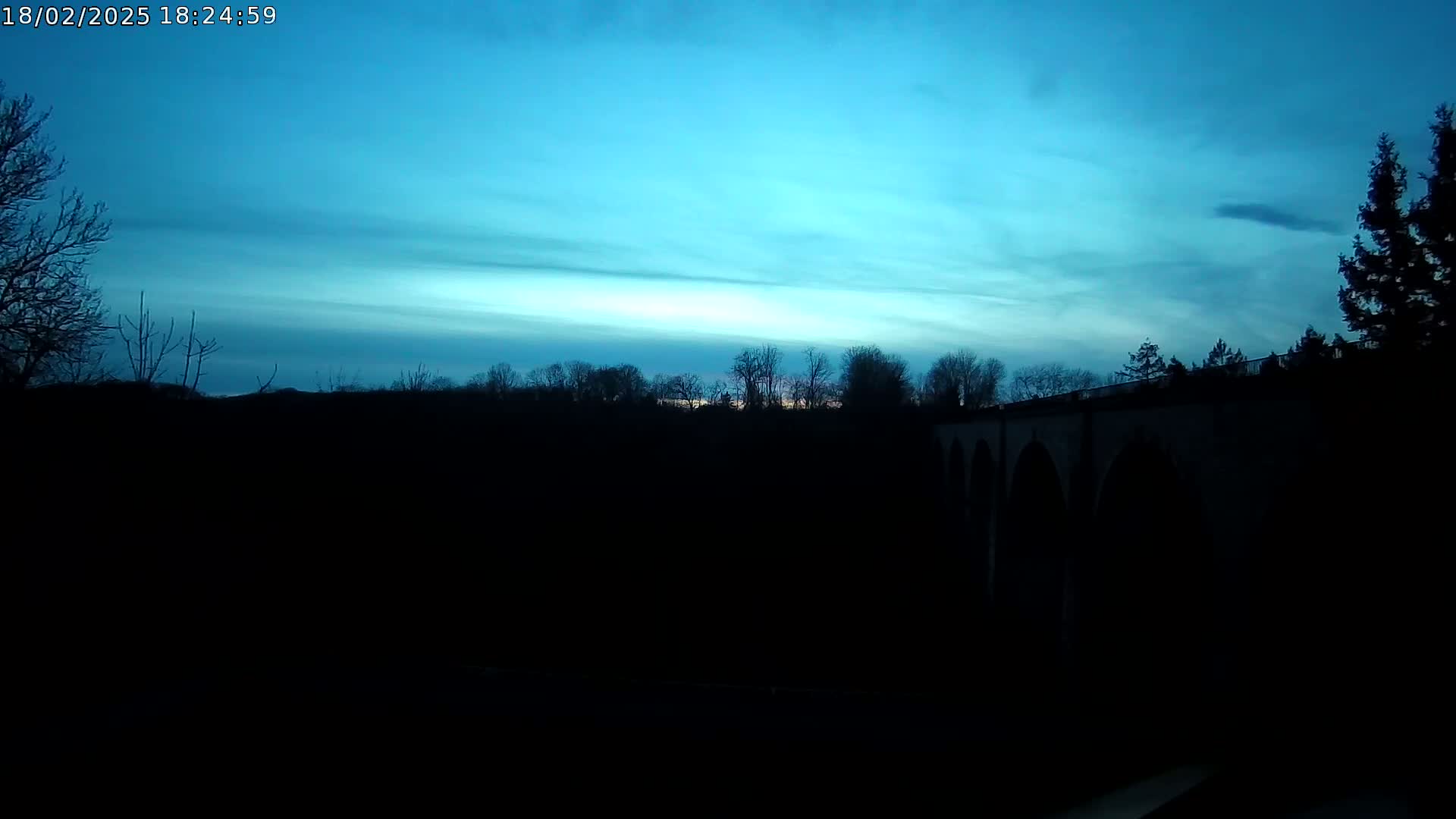 A dark silhouette of trees and a stone bridge is visible against a twilight sky showing streaks of light blue and a hint of lighter color near the horizon.