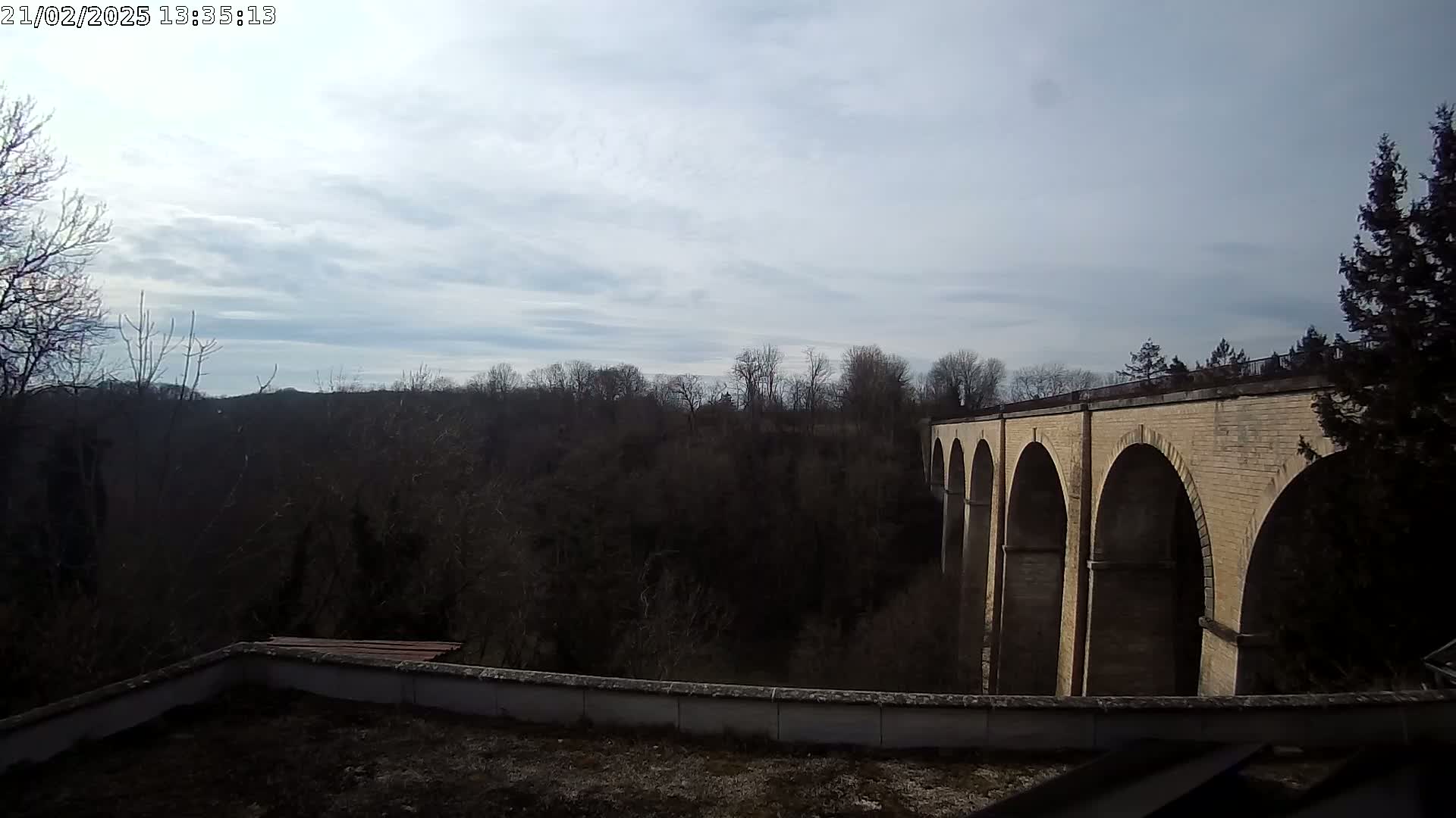 A brick viaduct spans a wooded valley under a partly cloudy sky.
